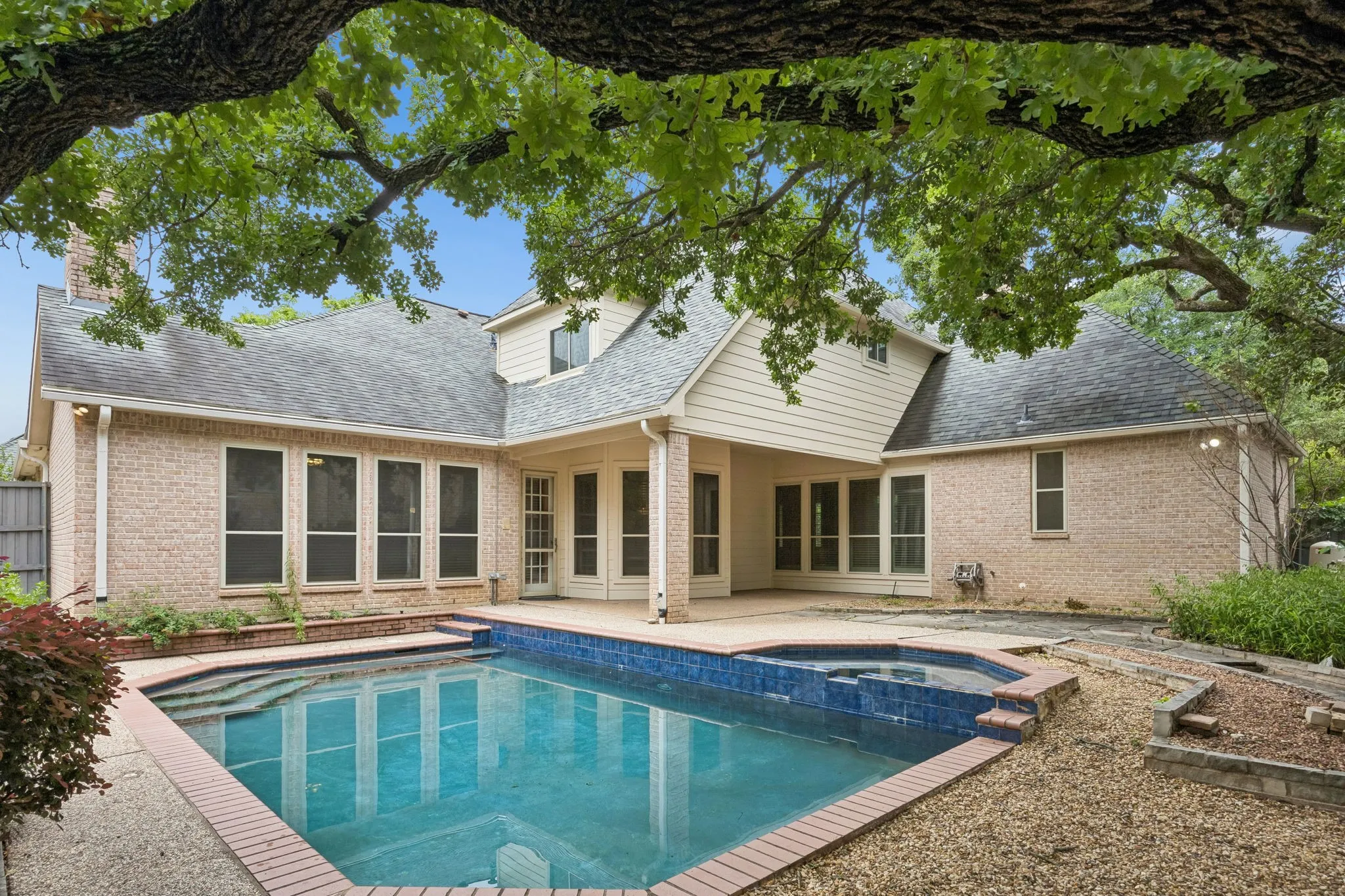 Backyard featuring an in-ground swimming pool with an integrated spa, brick coping, and a surrounding concrete patio