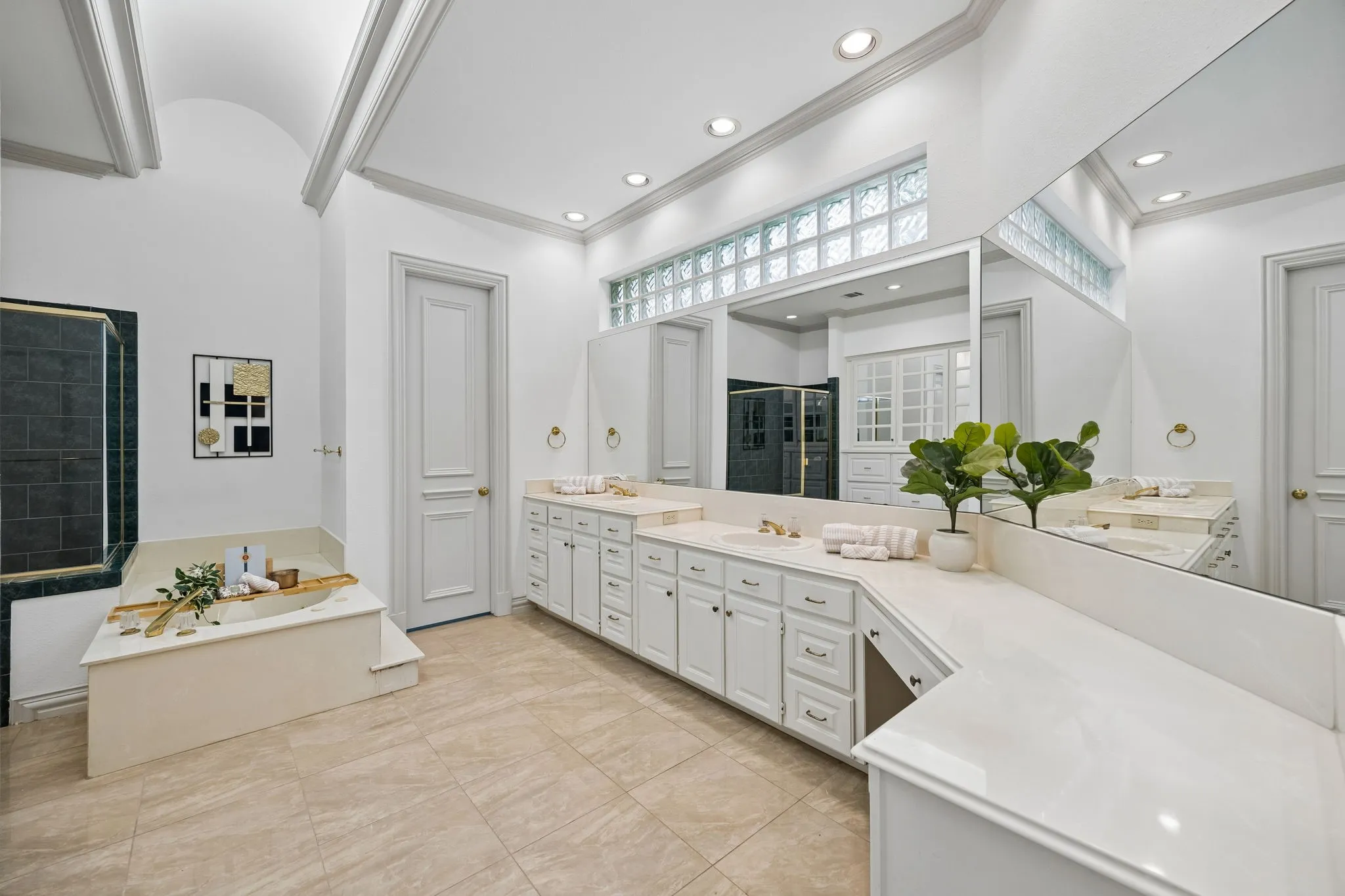 Spacious bathroom featuring a dual vanity with light-toned countertops, a built-in soaking tub, a separate glass-enclosed shower with dark tile, recessed lighting, and a vaulted ceiling with architectural beams