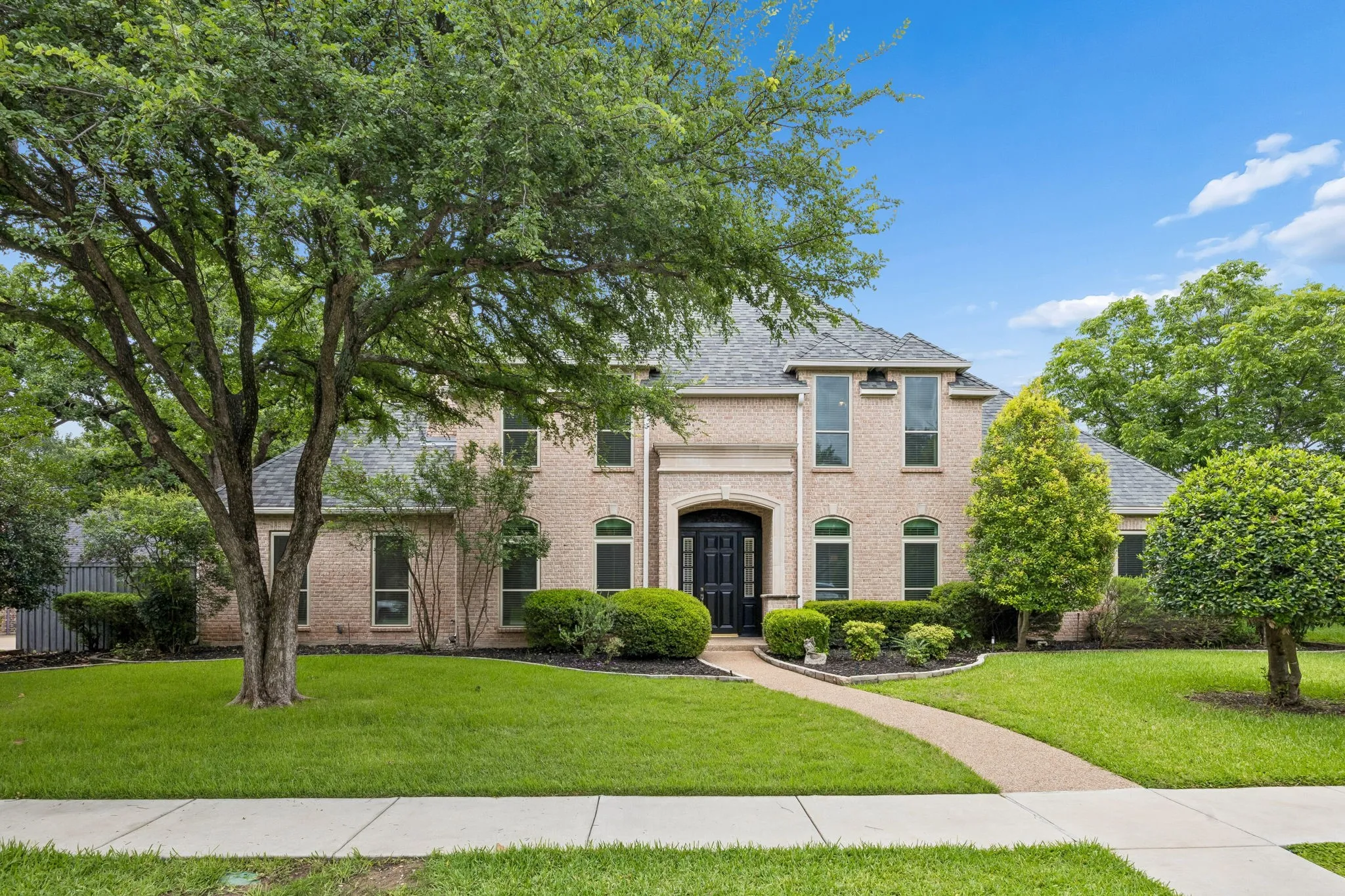 Two-story brick exterior featuring a multi-pane front door, arched and rectangular windows, a shingled roof, and a concrete pathway