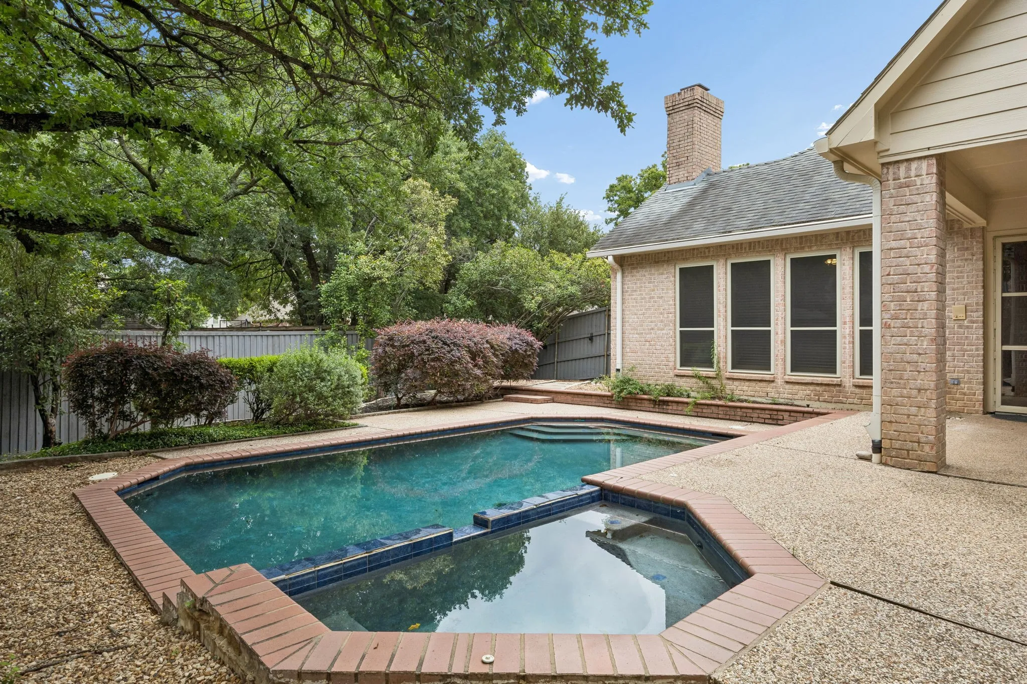 Backyard oasis featuring a swimming pool with integrated spa, brick coping, and an expansive exposed aggregate patio