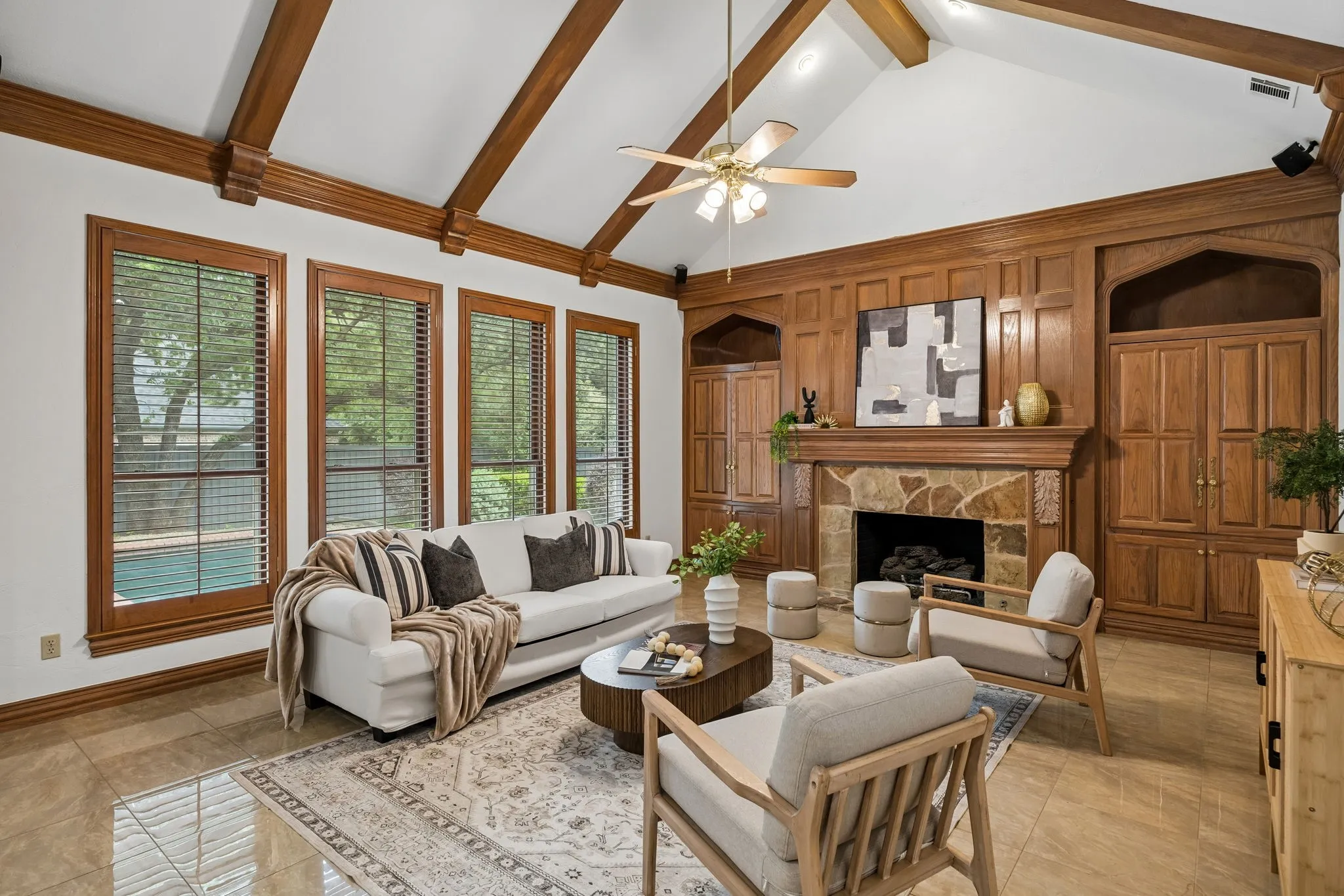 Vaulted ceiling with exposed wood beams, floor-to-ceiling wood paneling, stone-front fireplace, built-in cabinetry, and tile flooring