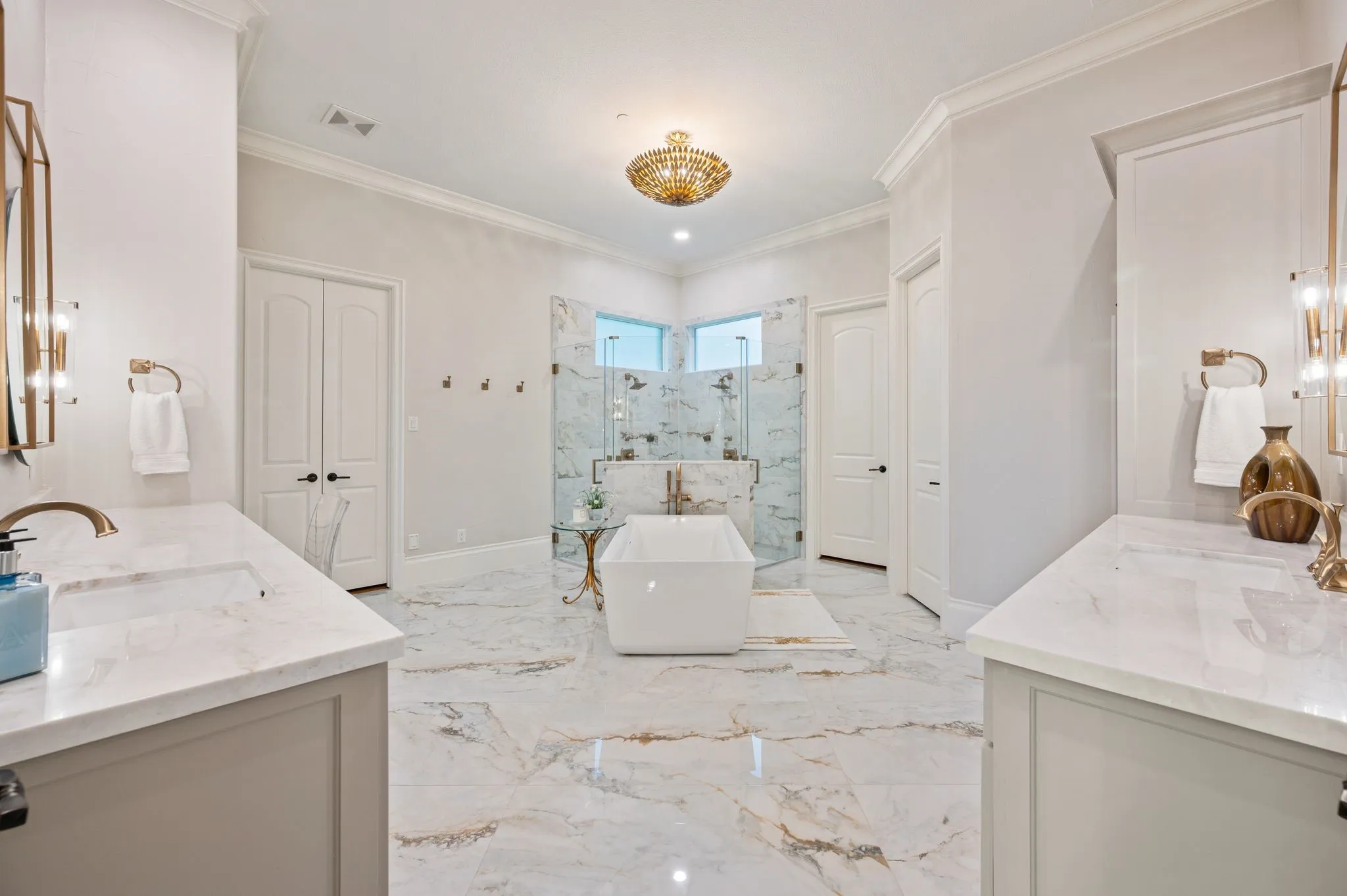 Truly luxurious primary bath with dual vanities, oversized shower, stand-alone tub & the most lovely tile surfaces designed with crisp, white-based tiles & surfaces with warm veining, and then accented with warm, lux gold hardware.