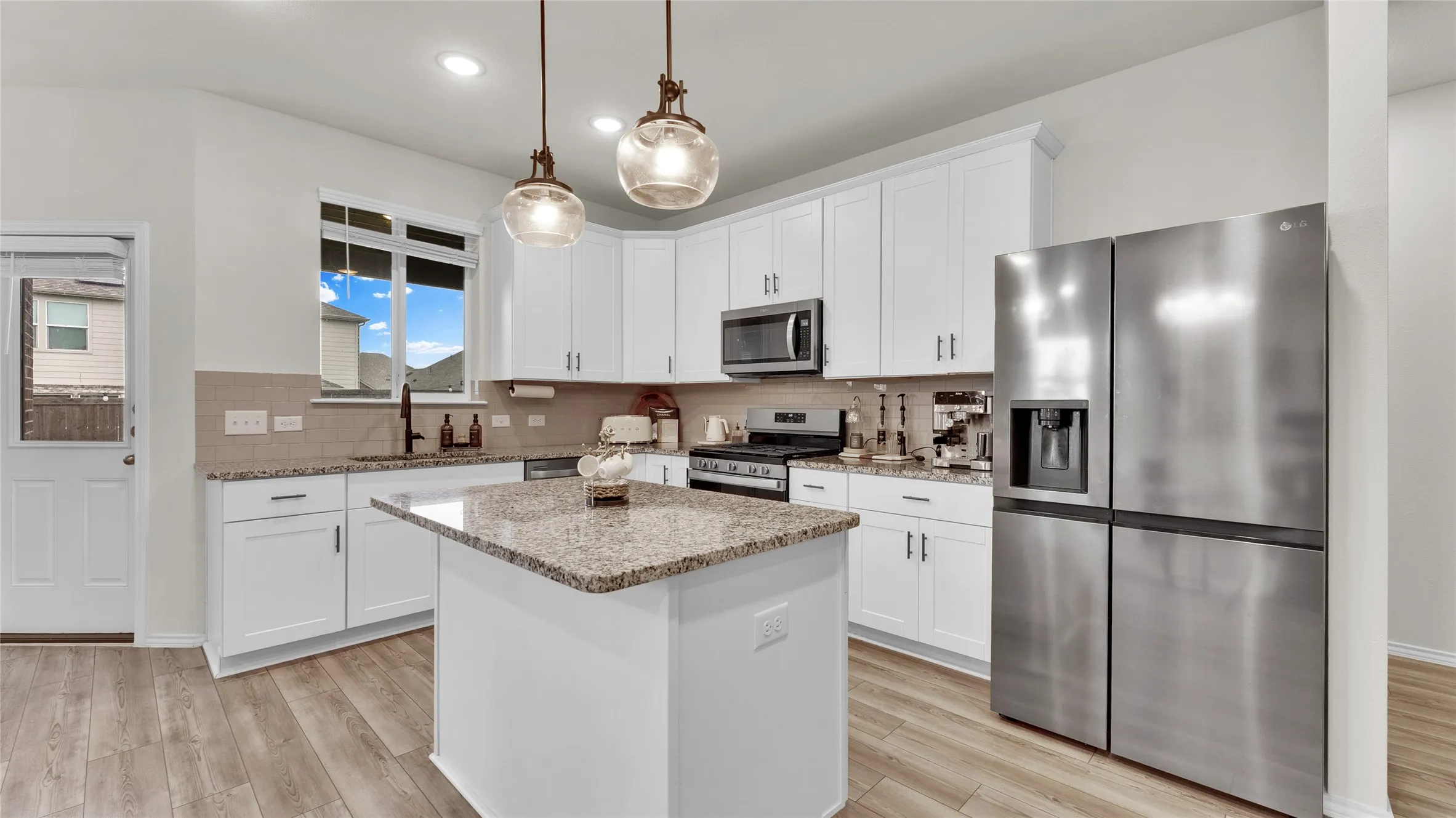Modern kitchen featuring an island with granite countertops, white cabinetry, stainless steel appliances, wood-finish flooring, and pendant lighting