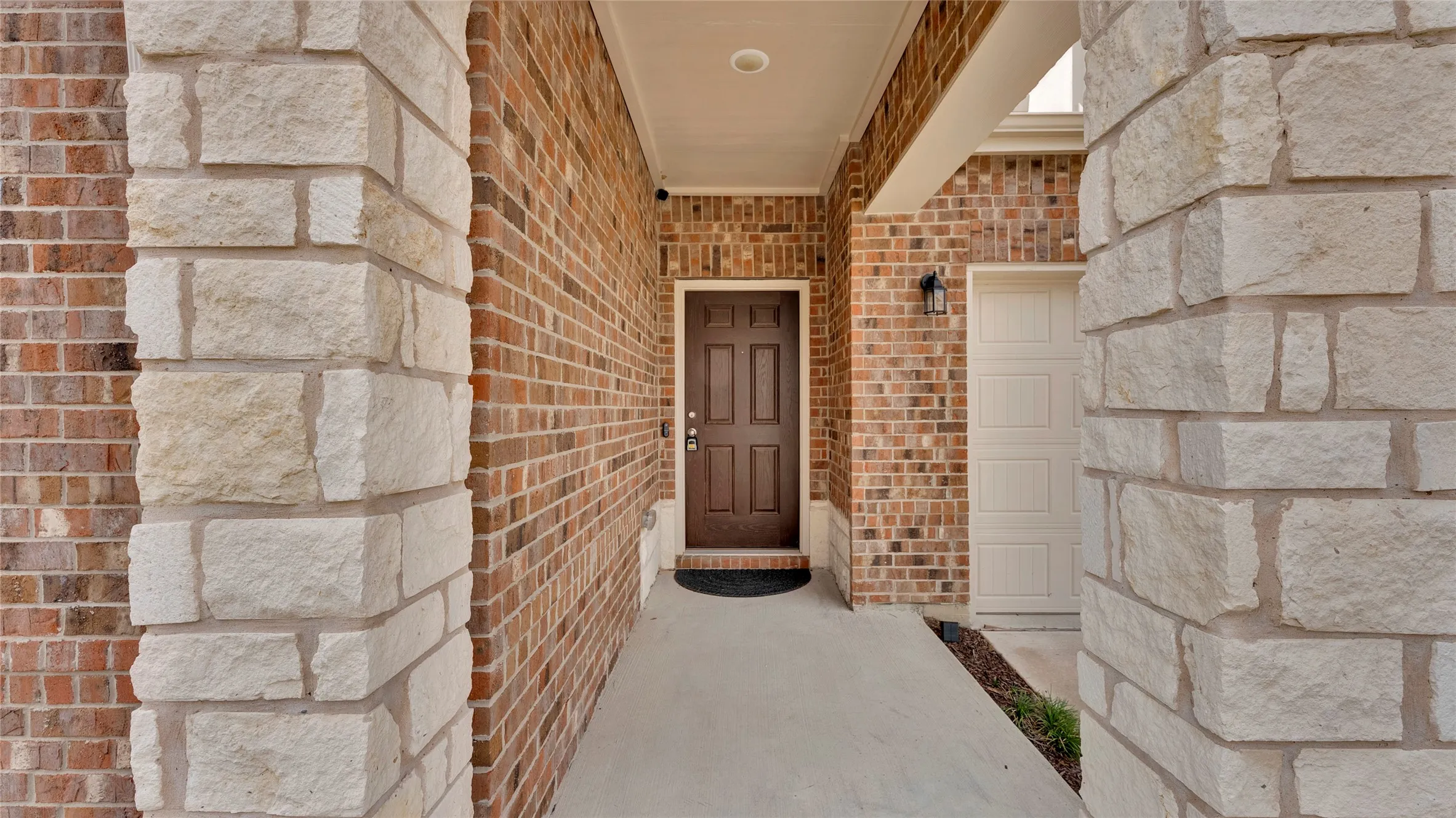 Exterior facade featuring a brown paneled entry door, light brick, stacked stone accents, and a panel-style garage door