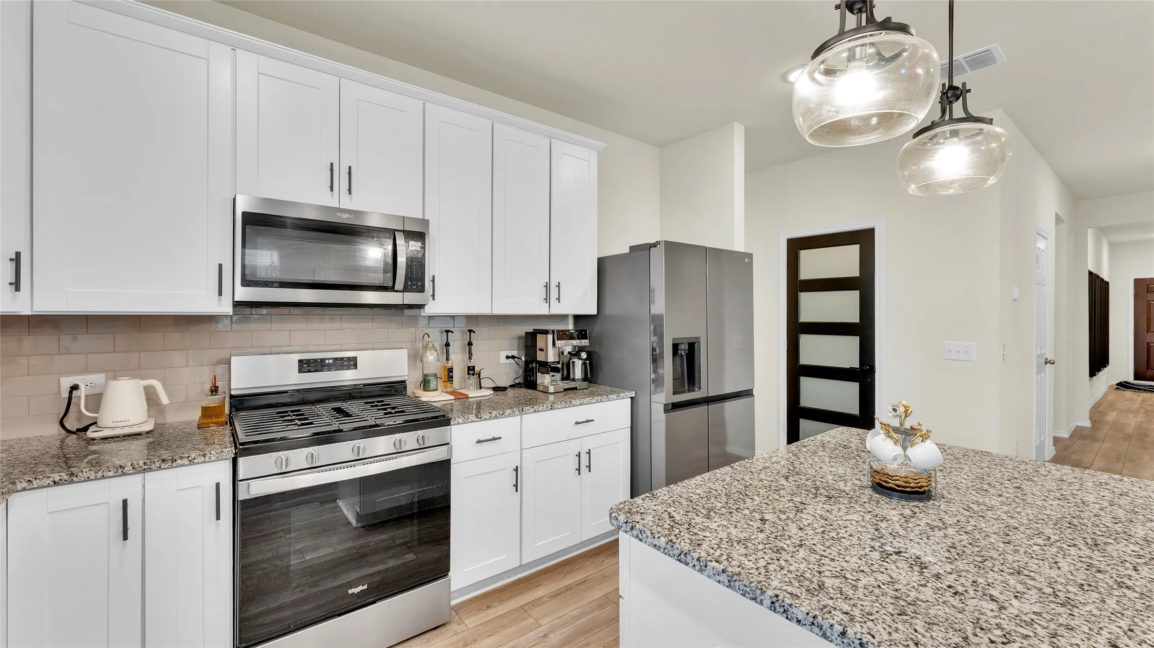 Modern kitchen featuring white shaker cabinetry, stainless steel appliances, speckled stone countertops, and a subway tile backsplash