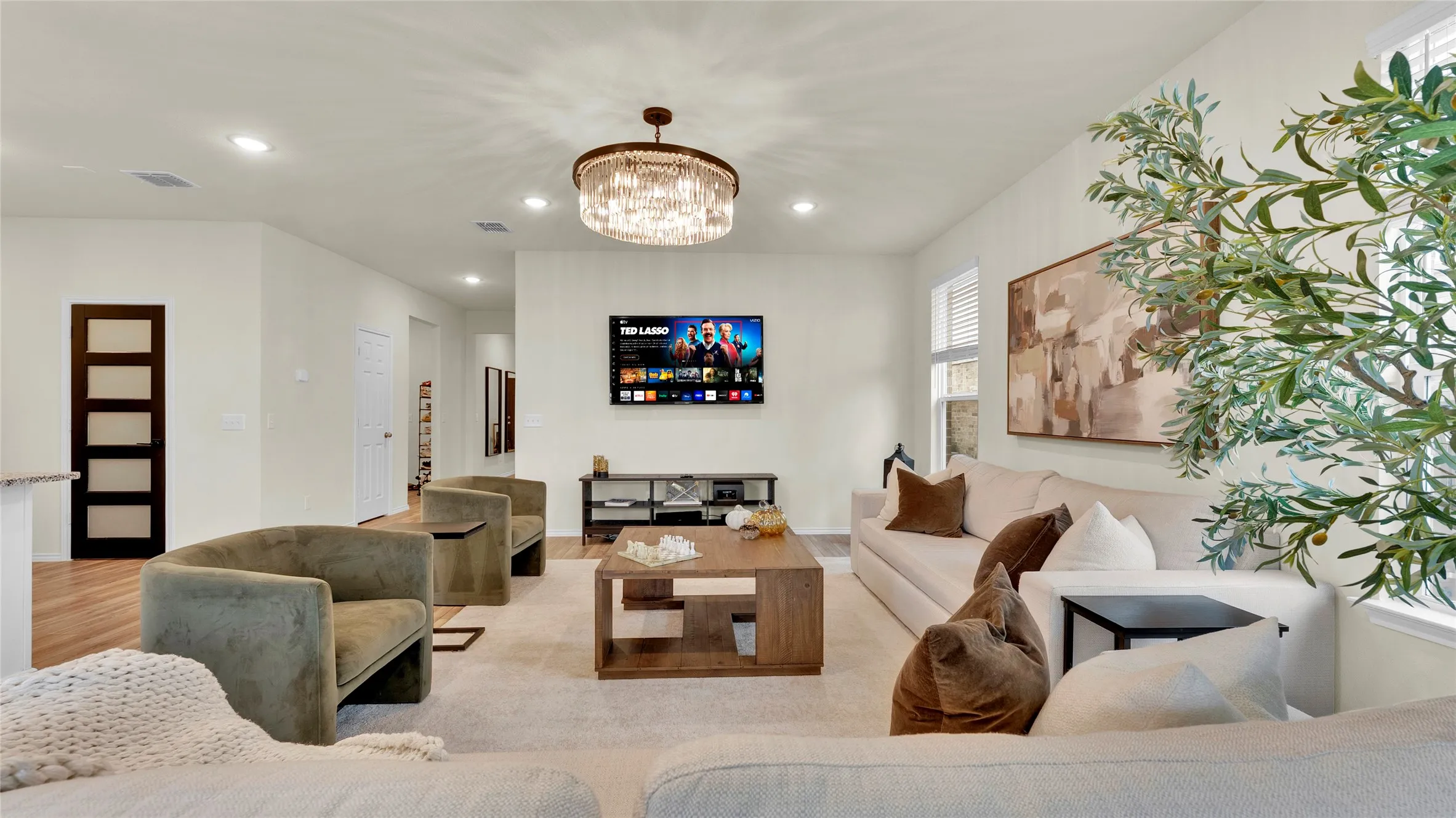 Expansive living area featuring recessed lighting, a contemporary chandelier, wood-finish flooring, and white walls