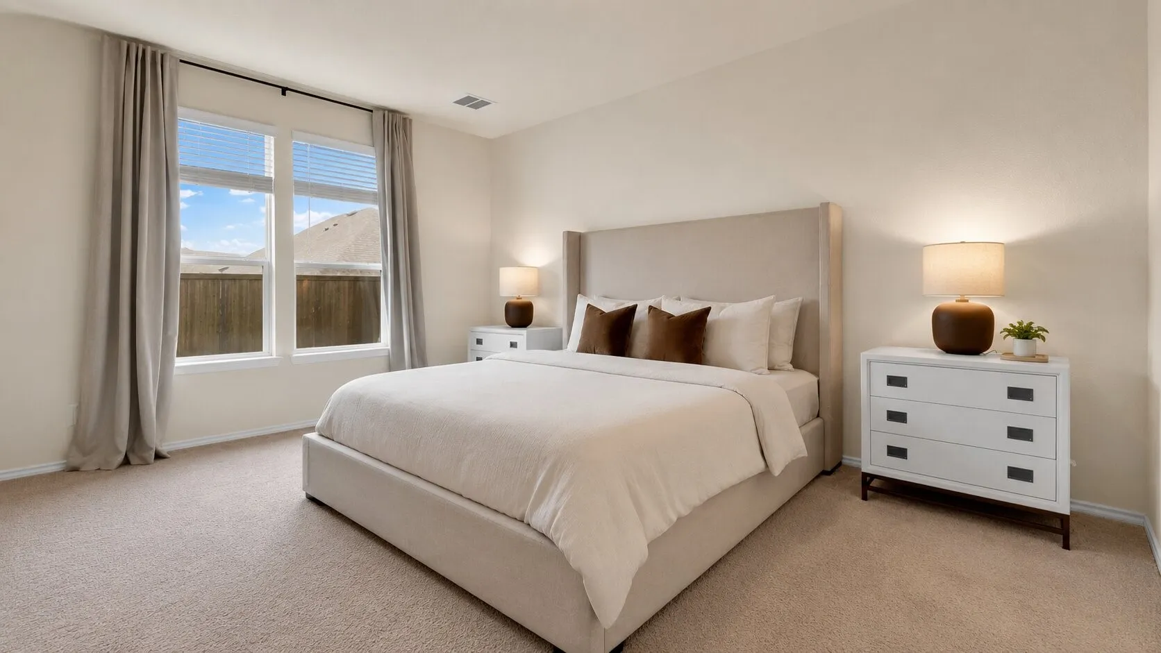 Spacious bedroom featuring light-colored carpet, large windows with blinds and drapery rods, and neutral wall tones