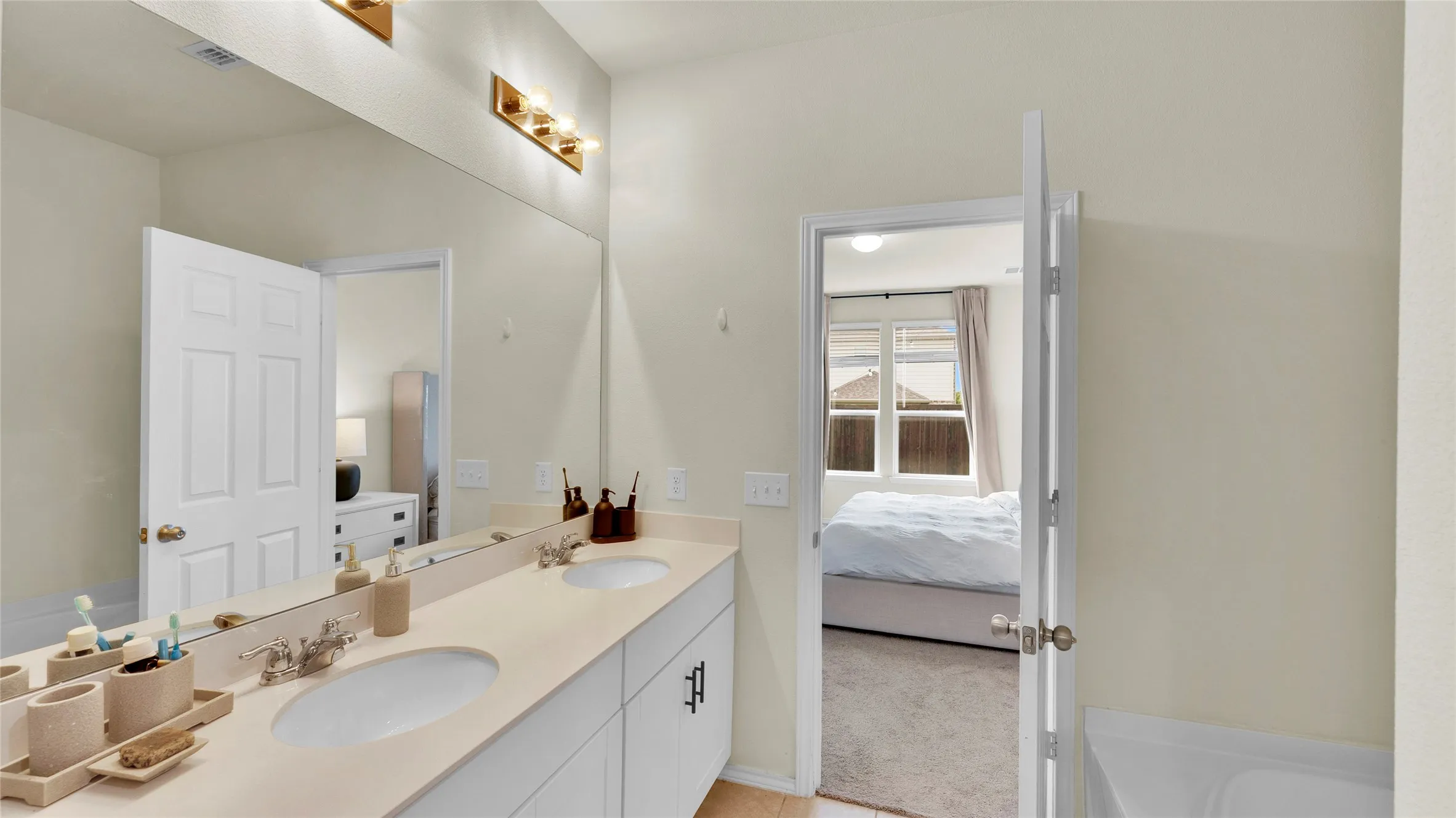Bathroom featuring a dual vanity with undermount sinks, a large mirror, and a three-light fixture