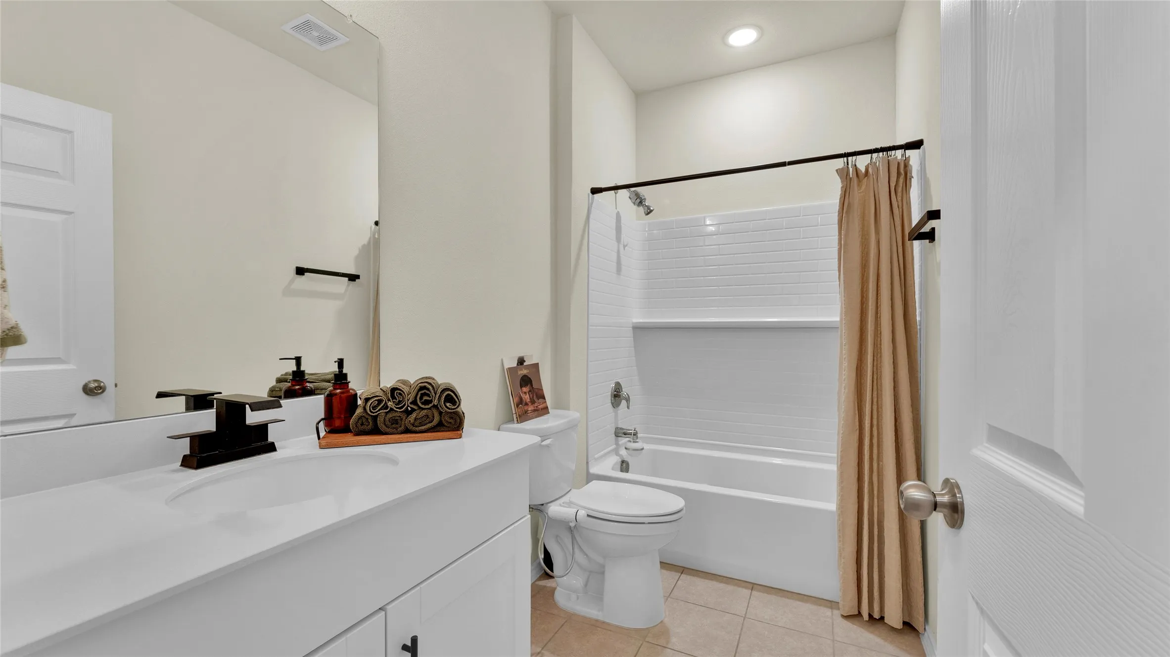 Bathroom featuring a white vanity with integrated sink, a rectangular mirror, a shower-over-tub combination with white subway tile surround, and neutral tile flooring