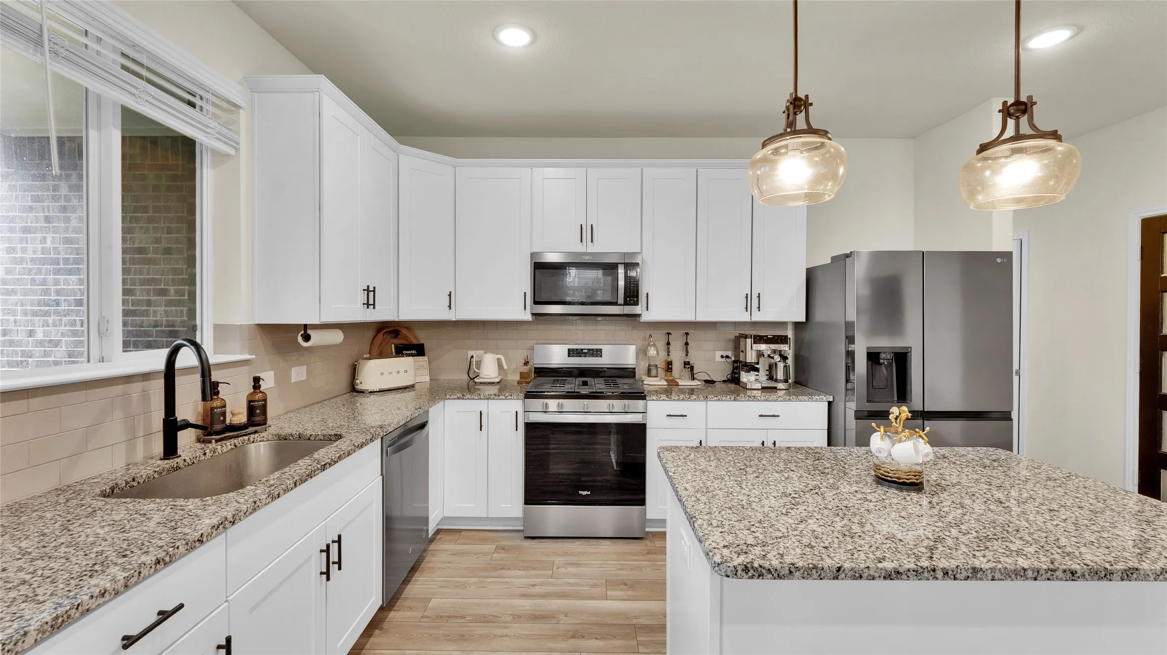 Contemporary kitchen featuring white cabinetry, stainless steel appliances, granite countertops, and wood-finish flooring