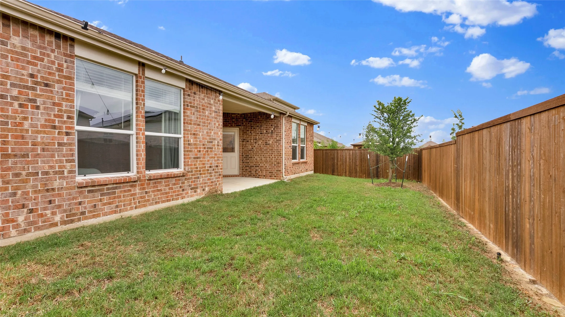 Private backyard featuring a covered patio, red brick exterior, wood privacy fencing, and a small tree
