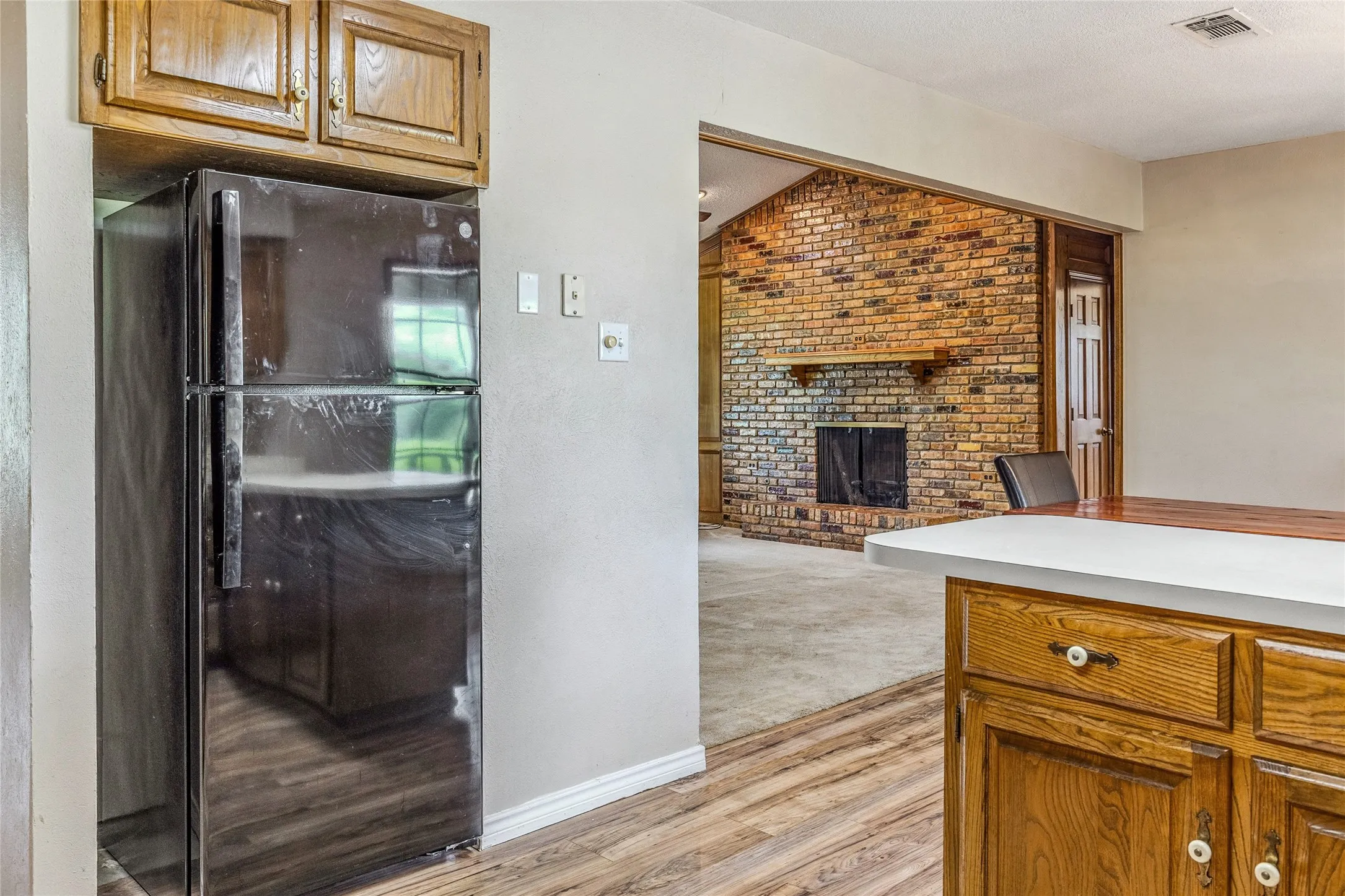 Kitchen area featuring wood-finish flooring, wood cabinetry with white knobs, and a dark refrigerator