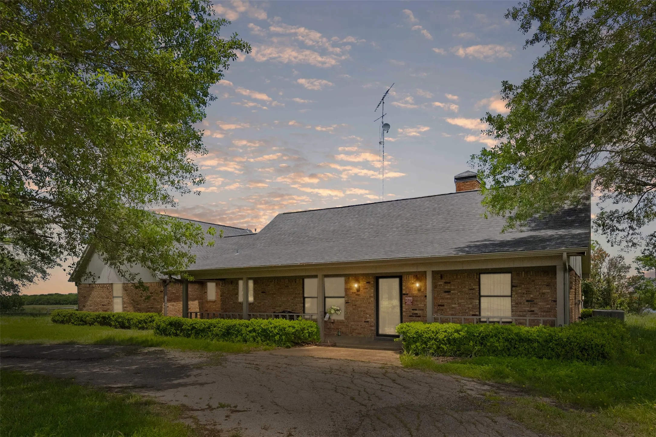 Brick exterior home featuring a covered front porch, dark asphalt shingle roof, and a prominent brick chimney