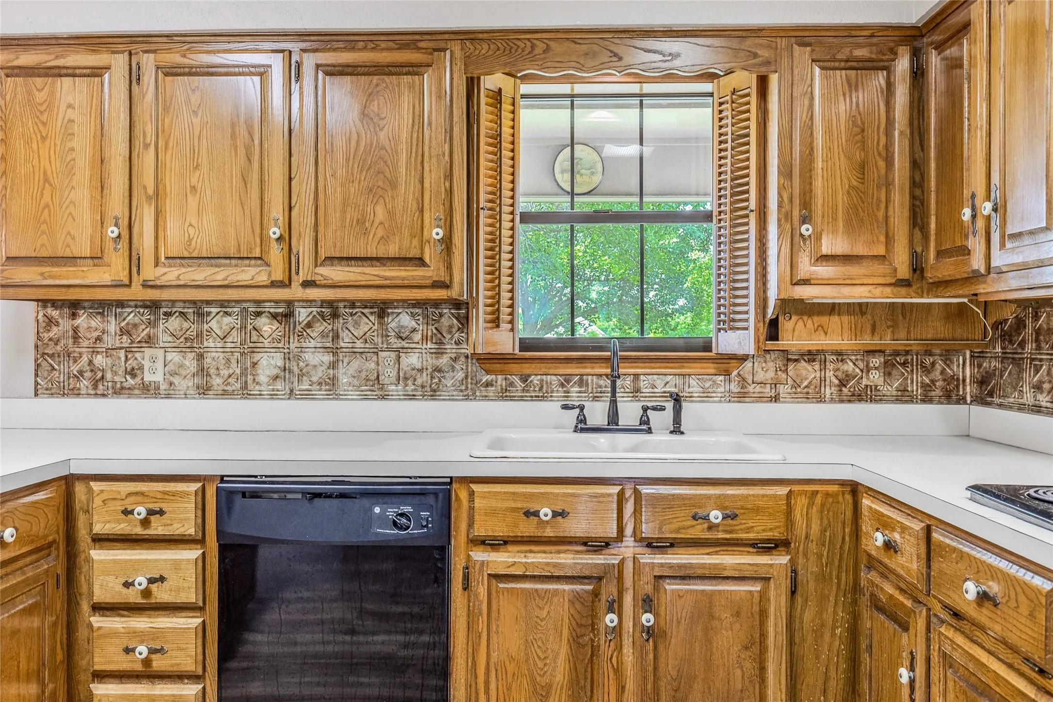 Wood-finish cabinetry with white knob hardware, white countertops, and a tiled backsplash
