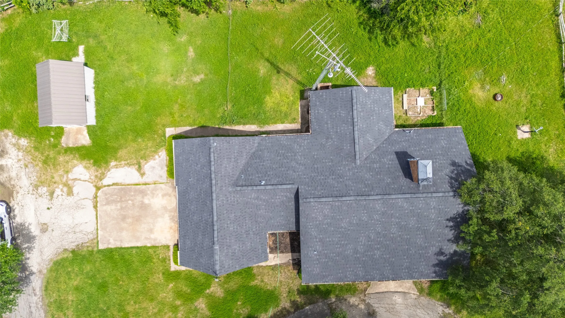 Expansive lot featuring a main residence with a dark shingle roof, a detached accessory structure, and a large grassy area