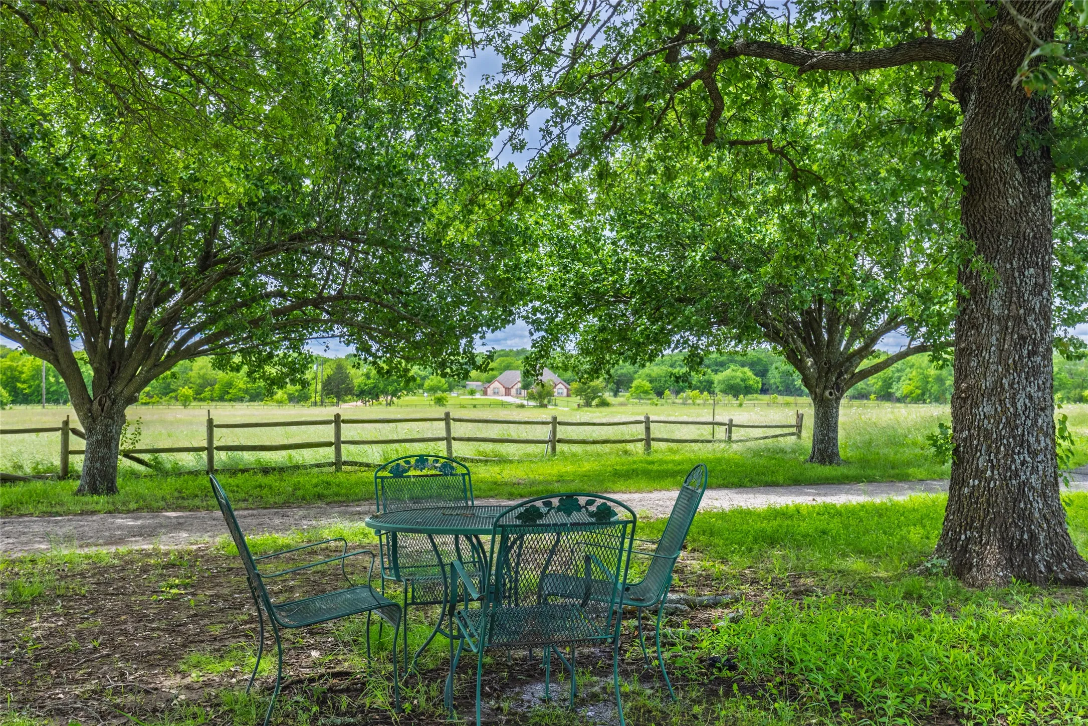 Expansive outdoor space featuring mature trees, a wooden split-rail fence, and a distant field