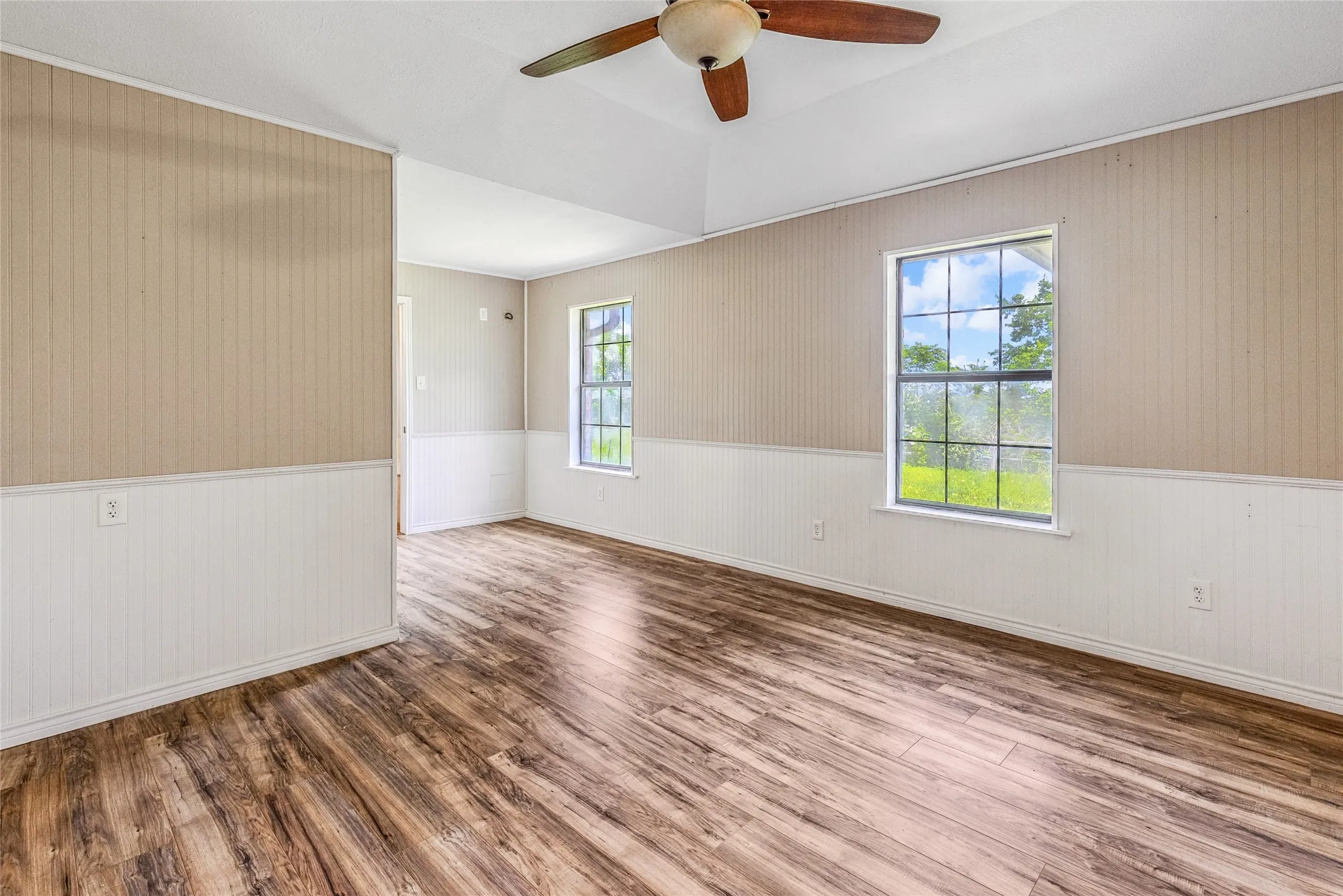 Spacious room featuring wood-finish flooring, two large windows, a tray ceiling, and a ceiling fan