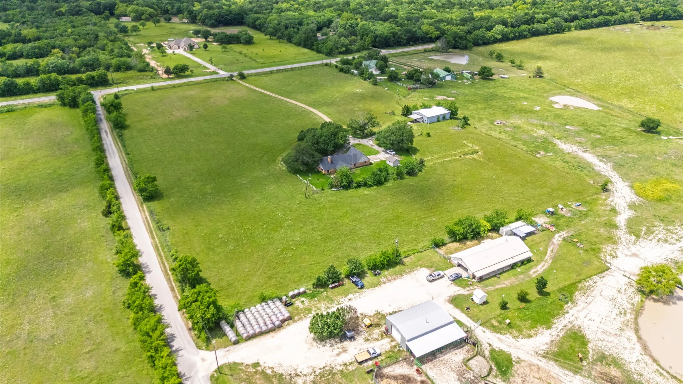 Expansive acreage featuring a main residence, multiple auxiliary buildings, paved road frontage, and varied terrain including open fields and wooded areas