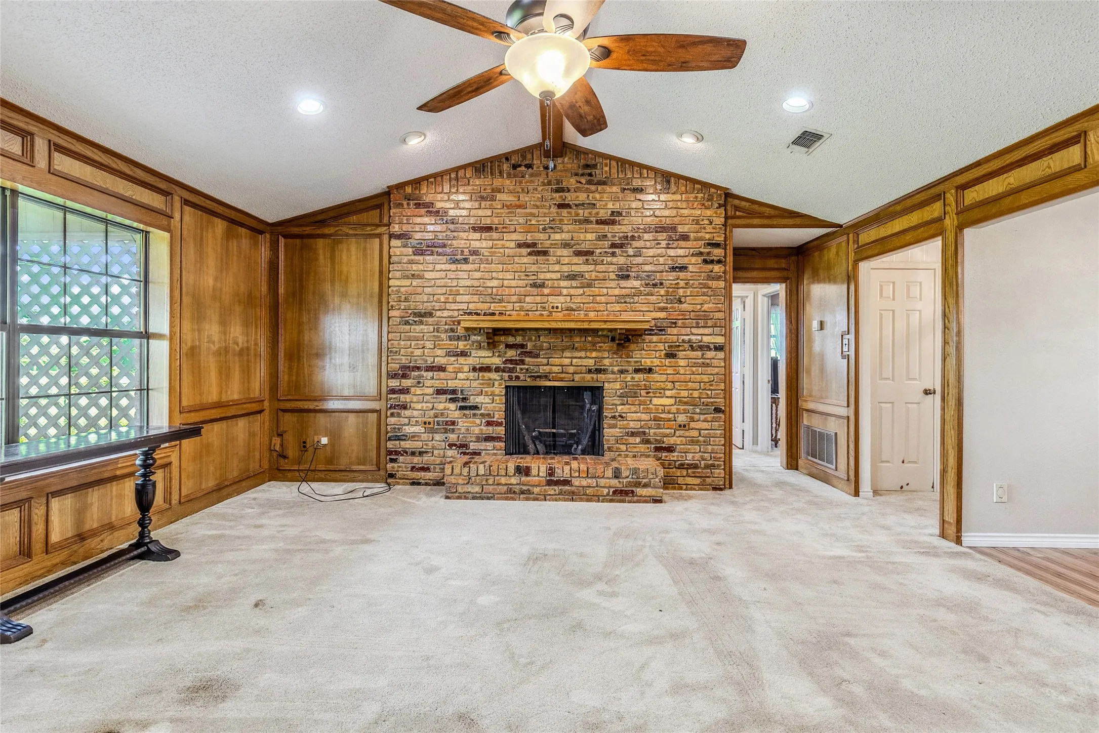 Exposed brick fireplace with a wood mantle, vaulted ceiling with recessed lighting, and a ceiling fan