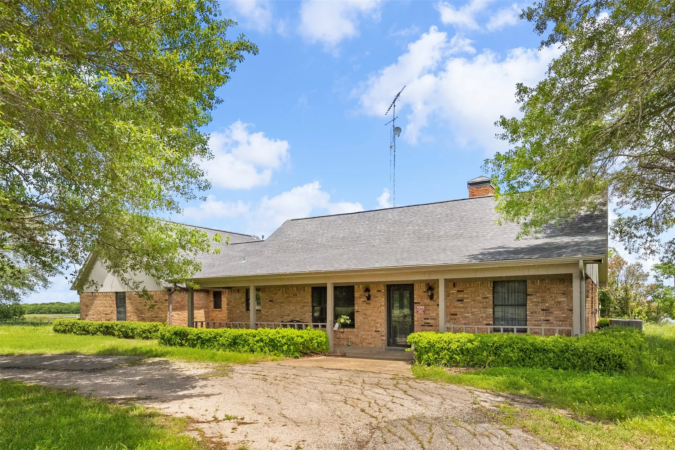 Brick exterior residence featuring a covered front porch, dark-framed entry door, and a shingle roof