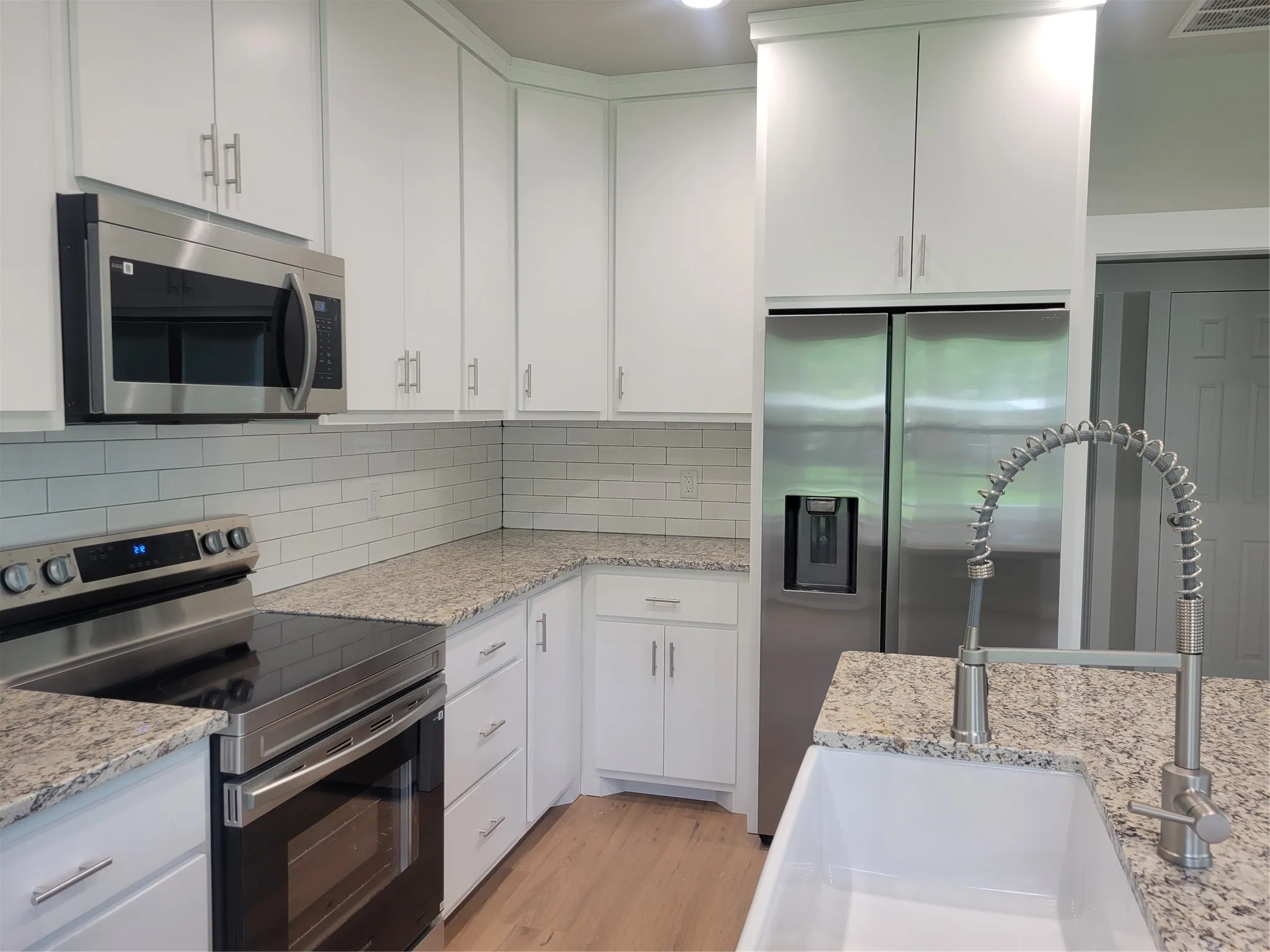 Modern kitchen featuring white shaker cabinetry, granite countertops, stainless steel appliances, subway tile backsplash, and a farmhouse-style sink with a pull-down faucet