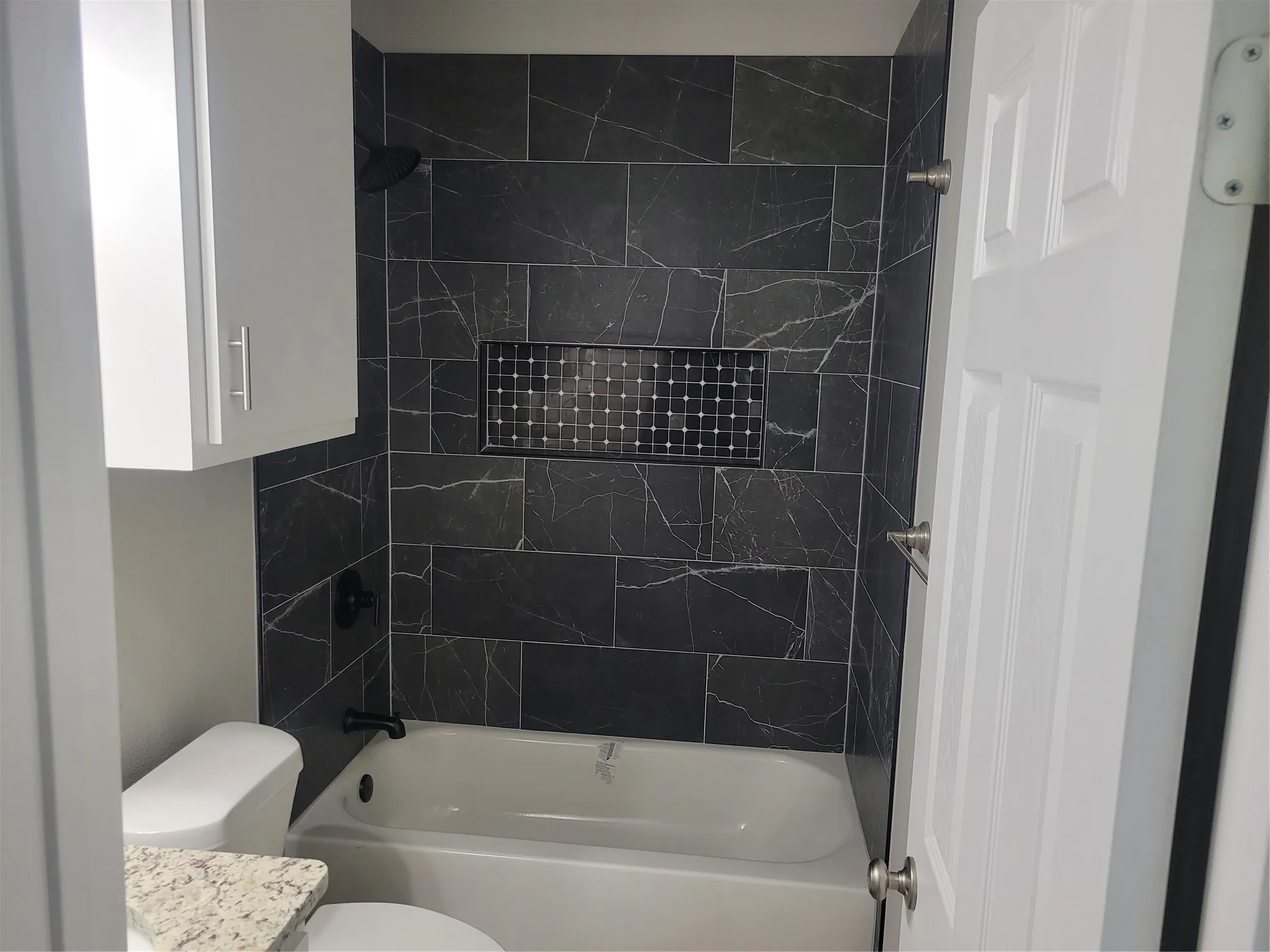Full bathroom featuring a white bathtub, dark tile surround with white veining, and a recessed shower niche with mosaic tile