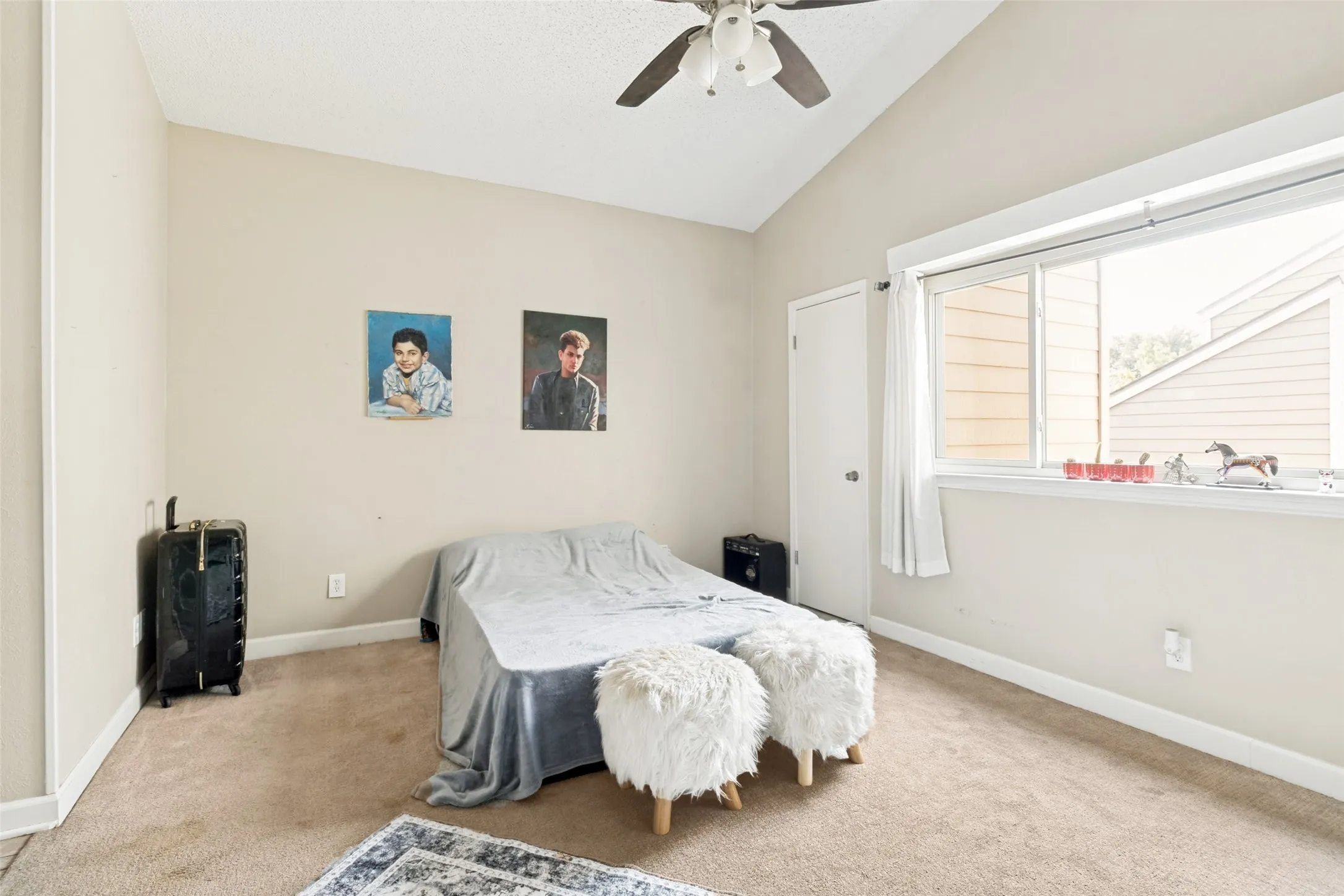 Carpeted room featuring a vaulted ceiling with a ceiling fan, a large window, and a white door