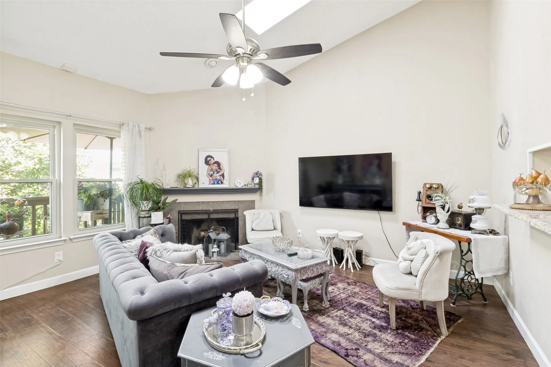 Living area featuring a vaulted ceiling with a ceiling fan, a fireplace with a stone surround and mantel, and wood-finish flooring