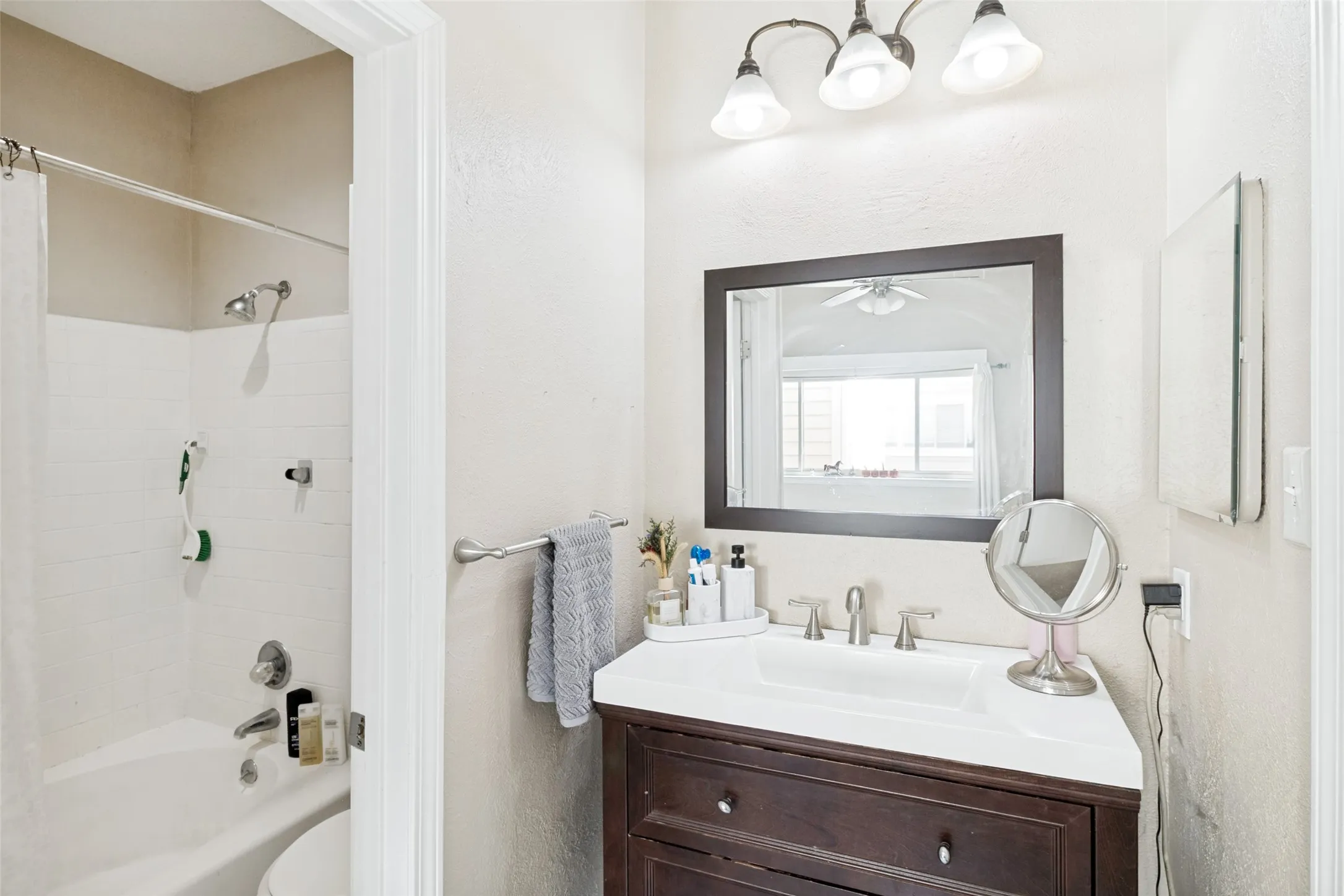 Bathroom featuring a dark wood-finish vanity with a white integrated sink, a framed mirror, and a three-light vanity fixture