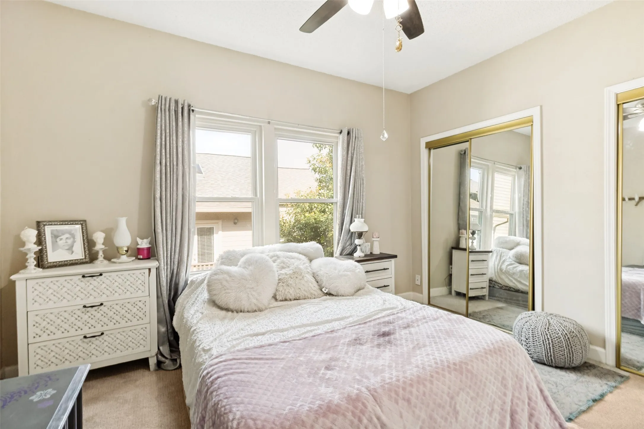 Carpeted bedroom featuring a ceiling fan, two windows with window treatments, and two mirrored sliding closet doors