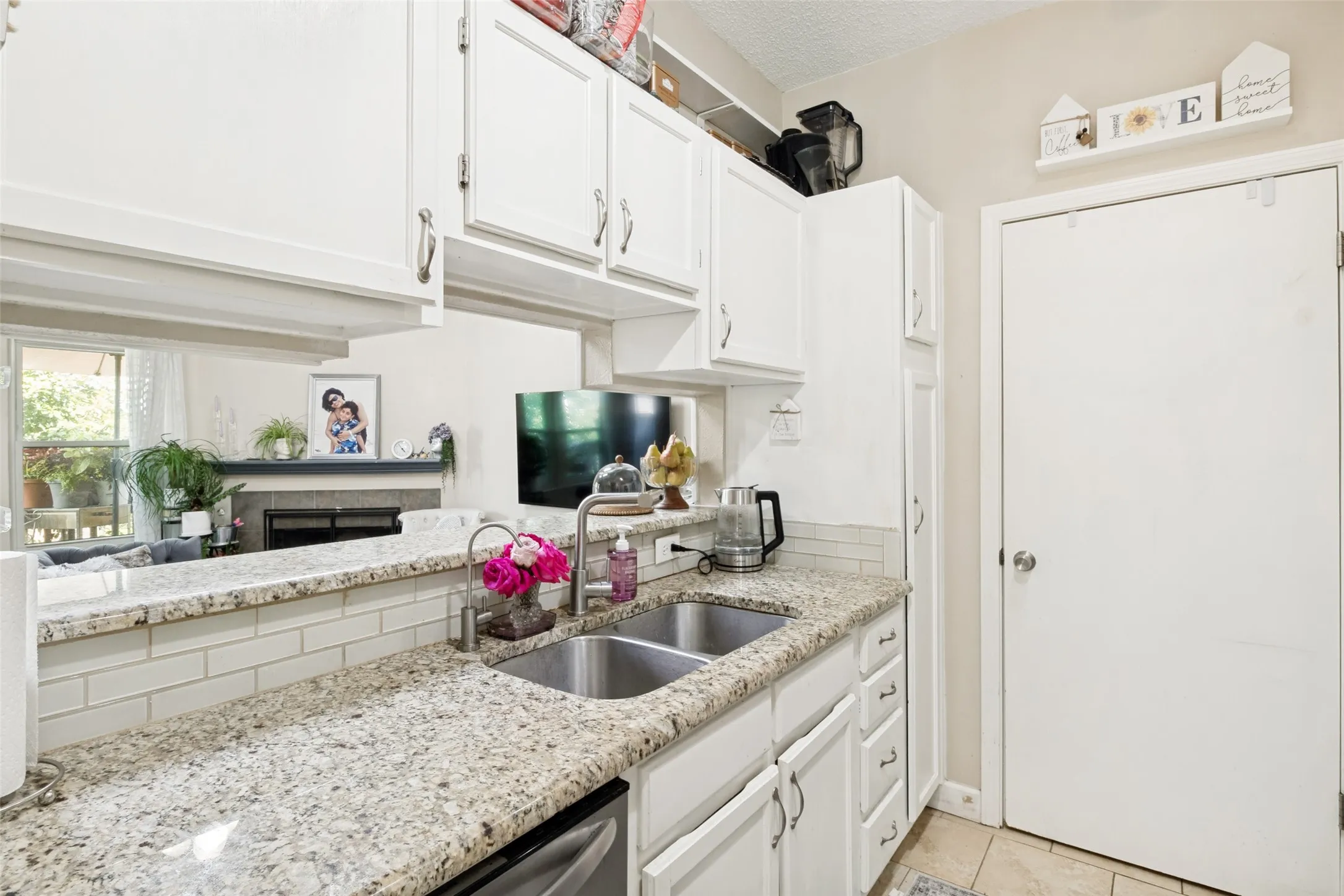 Kitchen featuring granite countertops, a double stainless steel sink, white cabinetry, and a subway tile backsplash