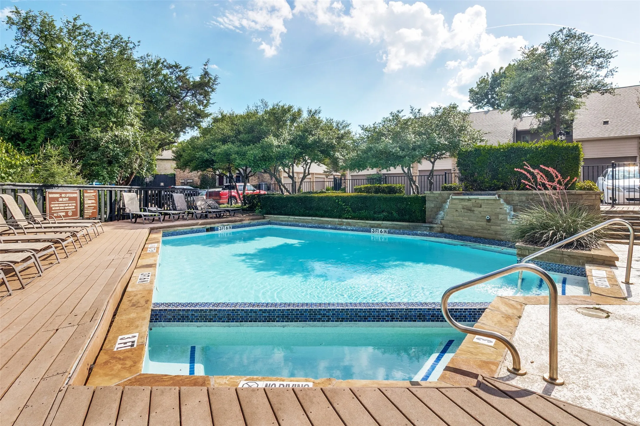 Outdoor swimming pool with a mosaic tile waterline and metal handrails