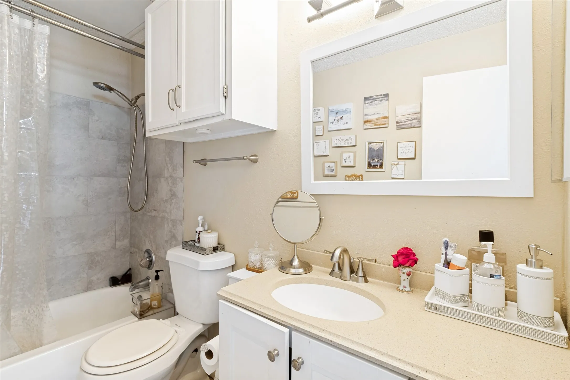 Bathroom featuring a tub/shower combination with light-toned tiled walls, a vanity with a light countertop, a white rectangular mirror, and white cabinetry