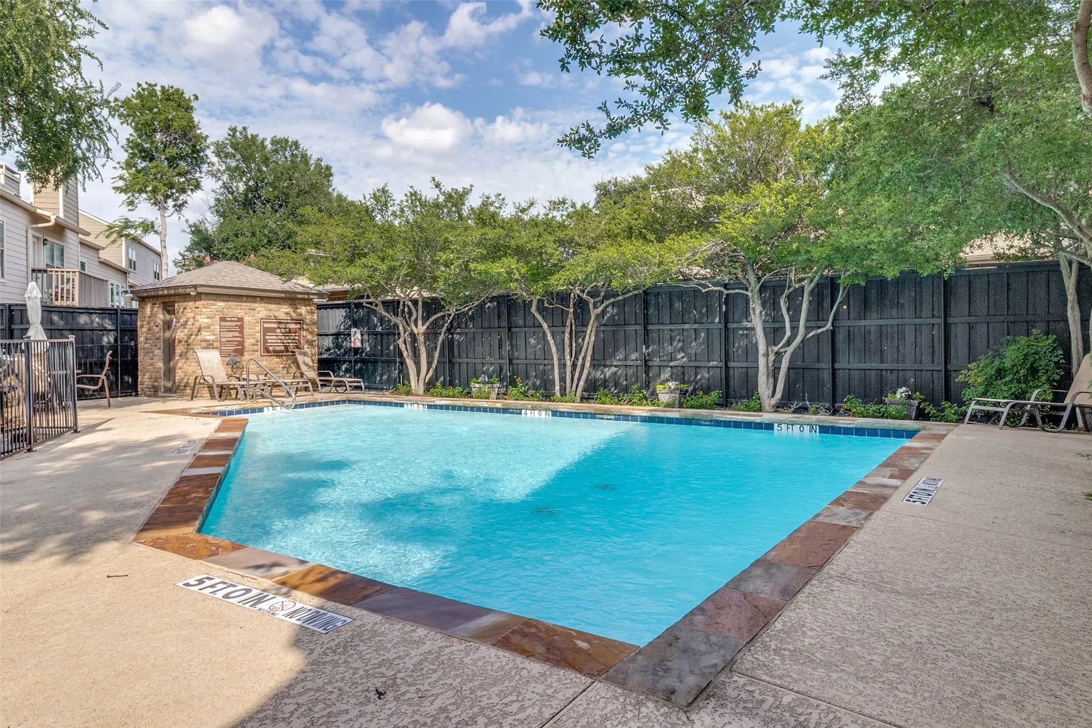 Swimming pool with tile coping, concrete decking, stone pool house, and privacy fencing