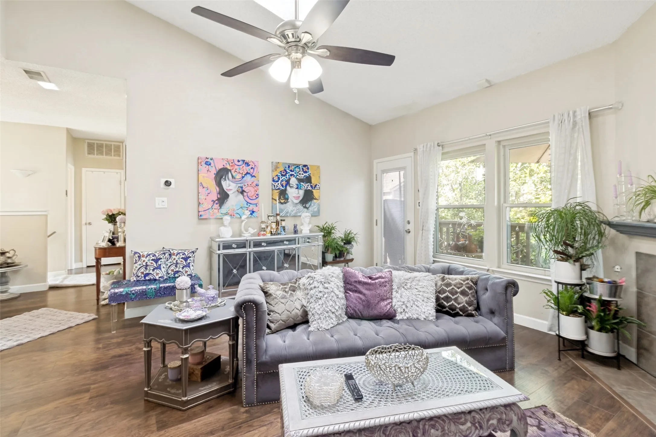 Spacious living area featuring vaulted ceilings, wood-finish flooring, a ceiling fan with integrated lighting, and multiple windows with a glass-paneled door providing natural illumination