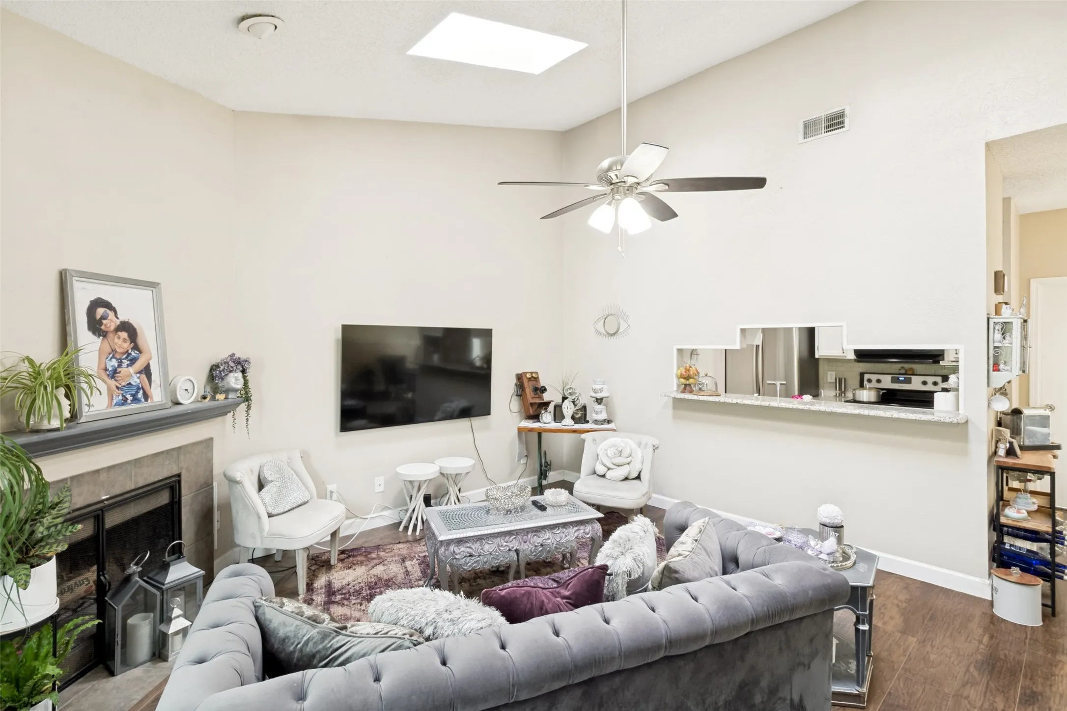 Living area featuring a vaulted ceiling with a skylight, wood-finish flooring, and a fireplace with a stone surround and mantel