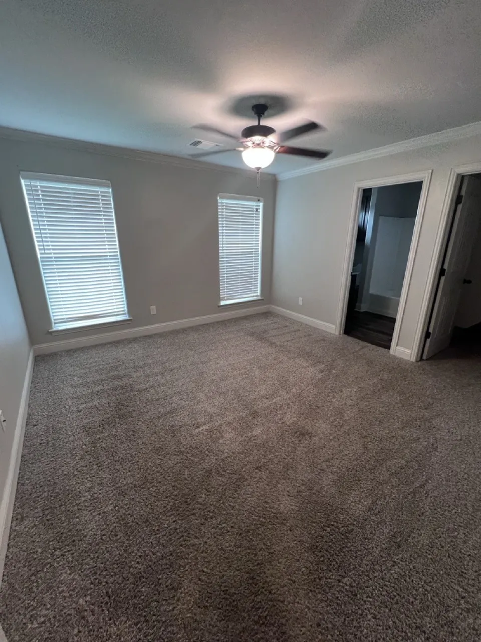 Spacious room featuring new carpet, two windows with blinds, a ceiling fan with integrated lighting, and crown molding