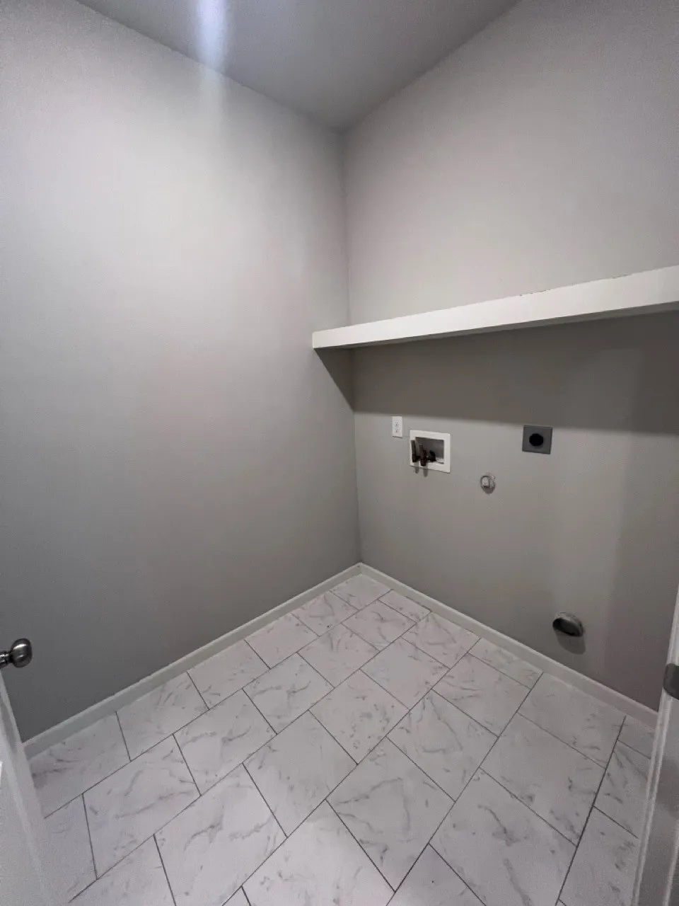 Dedicated utility space featuring light-toned walls and marble-look tile flooring