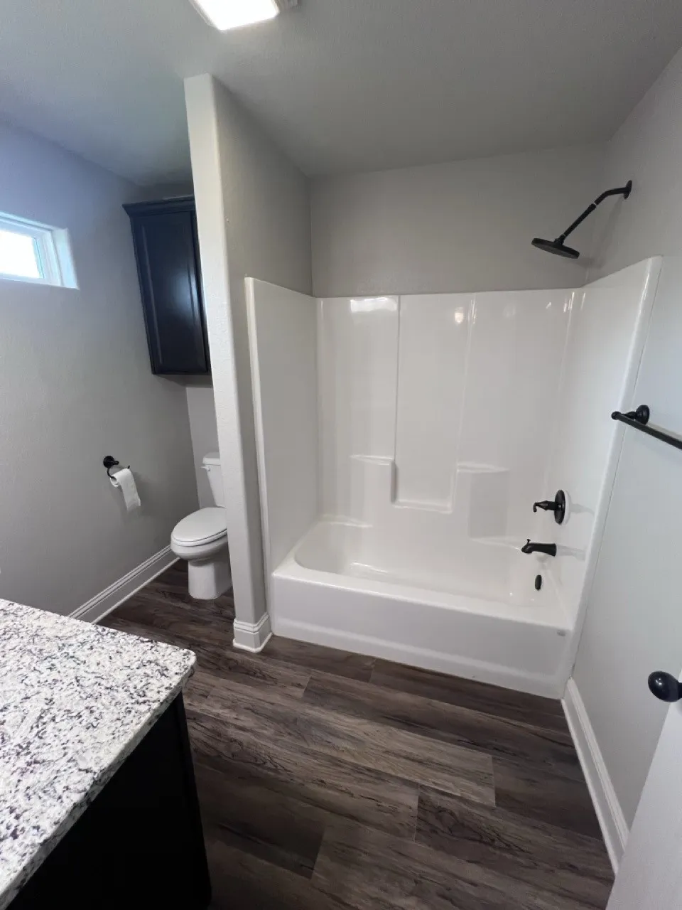 Bathroom featuring wood-finish flooring, a white tub and shower combination with dark-toned fixtures, and a vanity with a speckled countertop