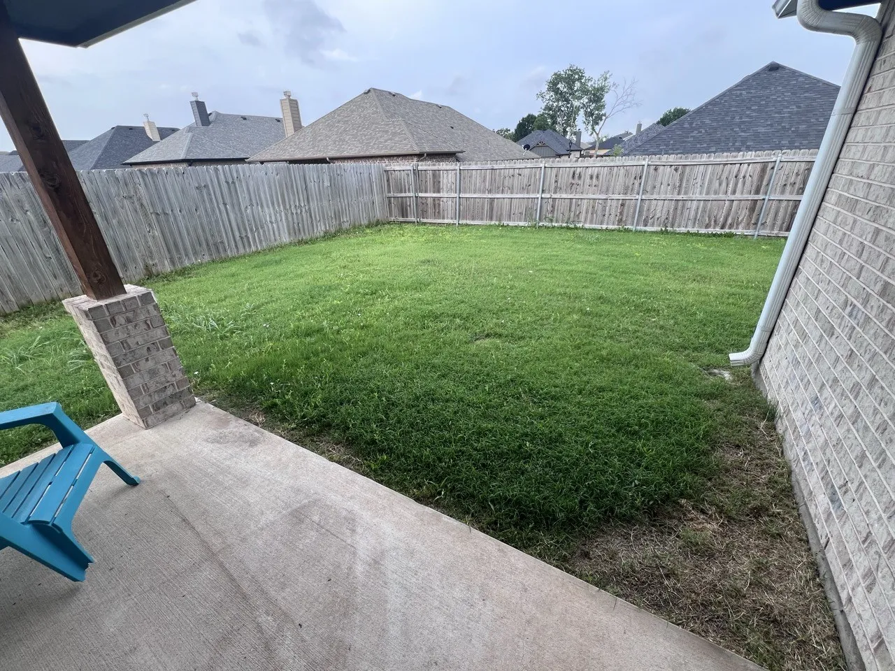 Expansive backyard featuring a lush green lawn, full wood privacy fencing, and a concrete patio with a brick-clad support column