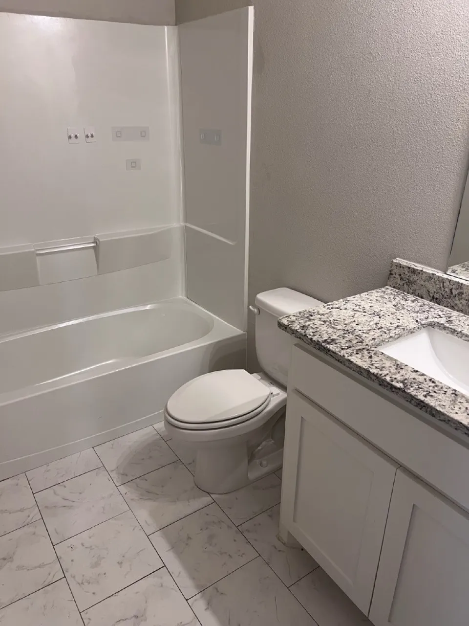 Bathroom featuring a white bathtub, ceramic tile flooring, a white vanity with shaker-style cabinetry, and a speckled countertop with an integrated sink