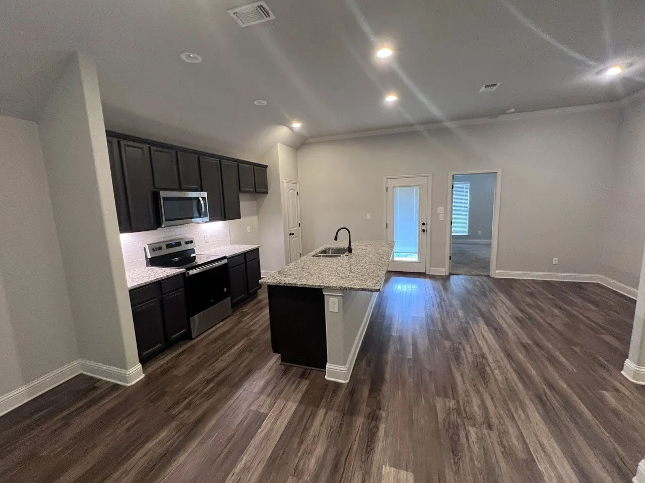 Modern kitchen with dark wood-finish cabinetry, stainless steel appliances, and a central island featuring a granite countertop