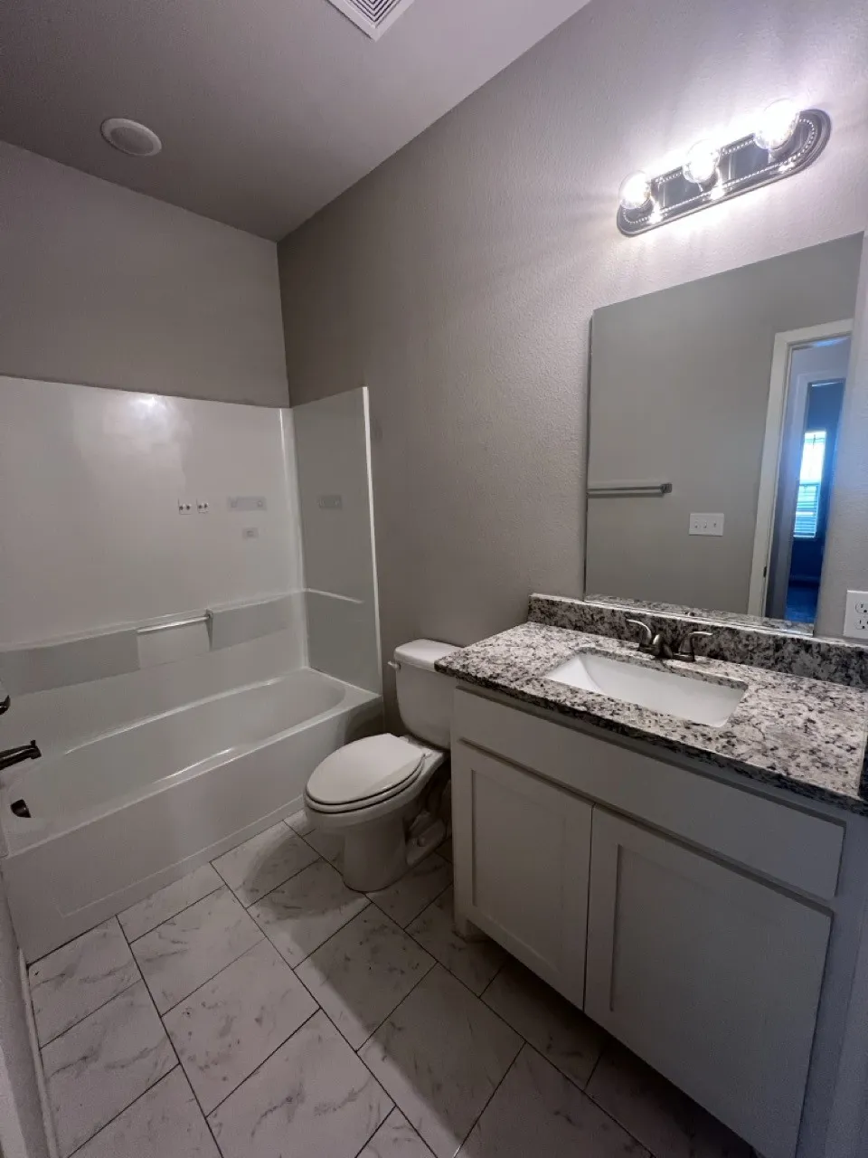 Bathroom featuring a white bathtub, a toilet, and a vanity with a granite-look countertop