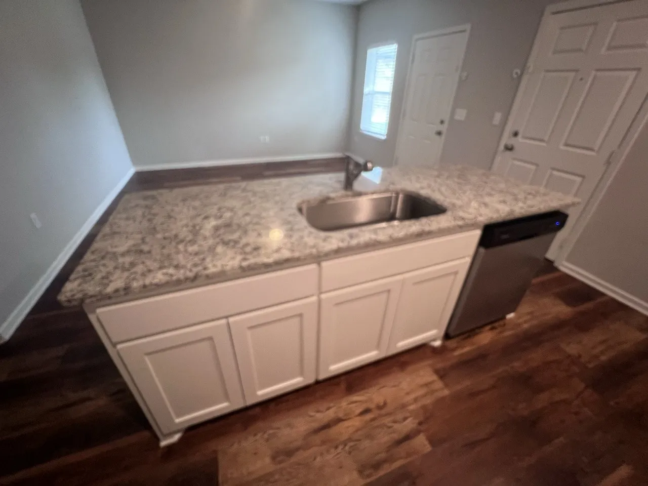 Kitchen island featuring a stainless steel sink, granite countertop, white shaker-style cabinetry, and integrated stainless steel dishwasher