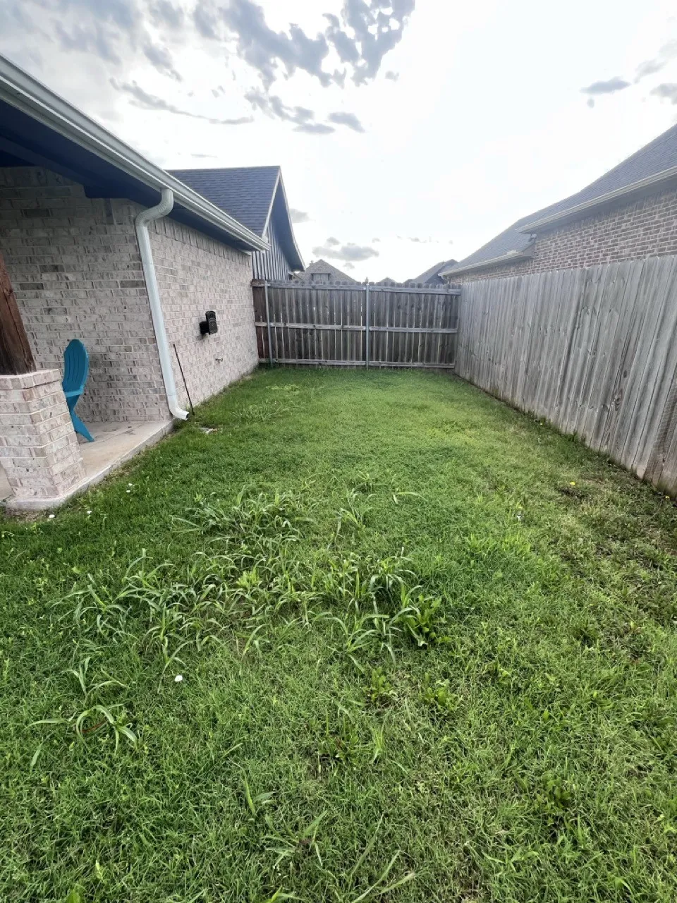 Expansive grassy area featuring a wood fence, concrete patio, and brick exterior