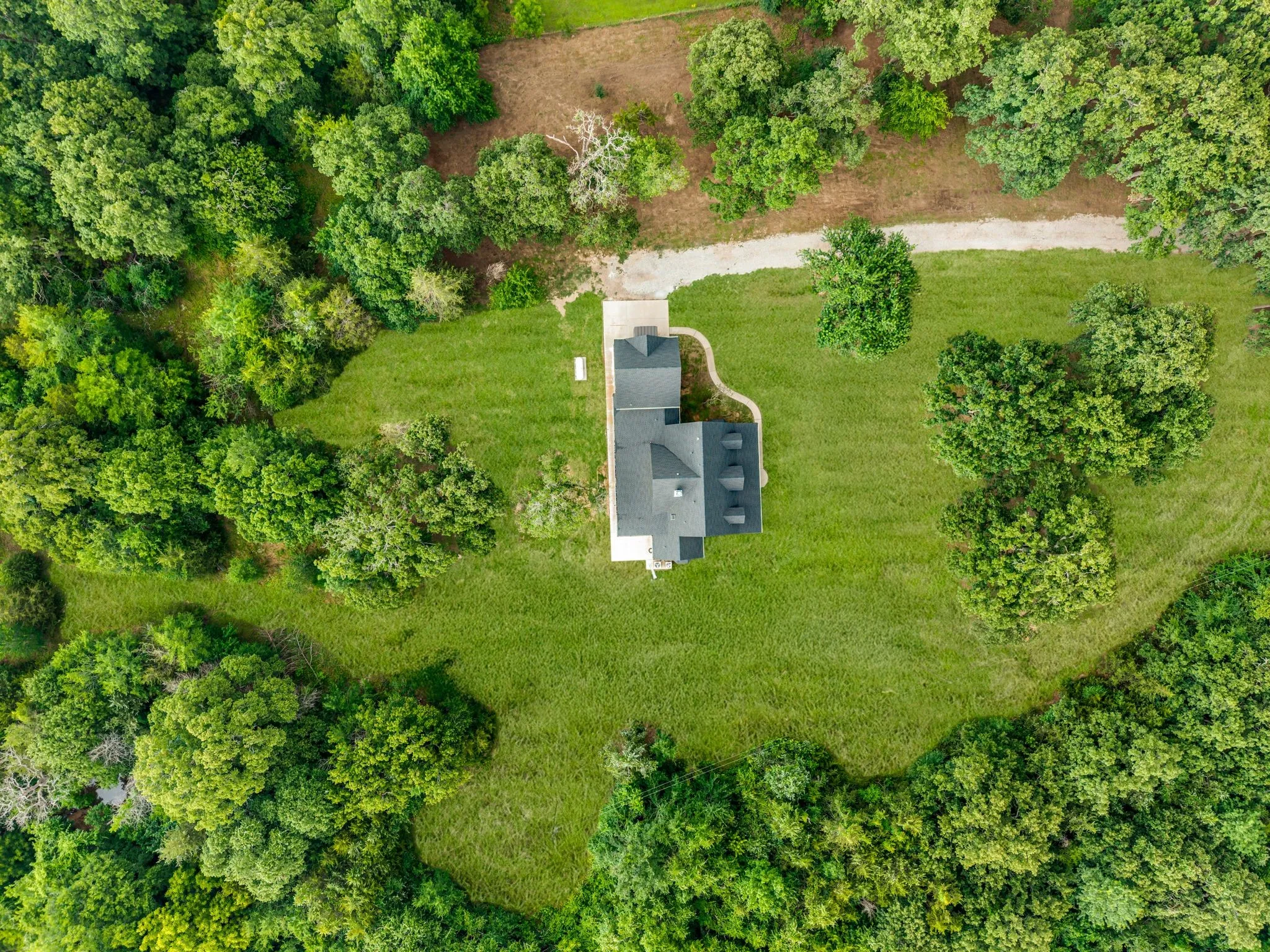Aerial property overview showcasing a central residence with a dark-pitched roof and a light-colored driveway