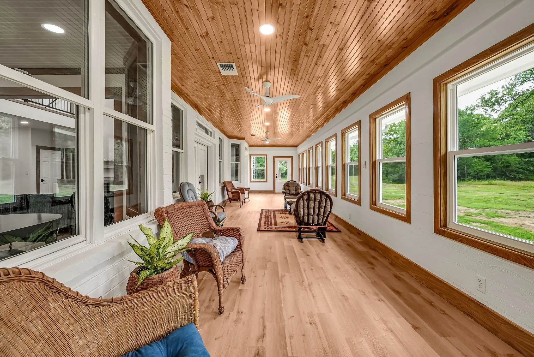 Spacious sunroom featuring a natural wood plank ceiling, light wood-finish flooring, white walls, and a series of large windows with natural wood trim