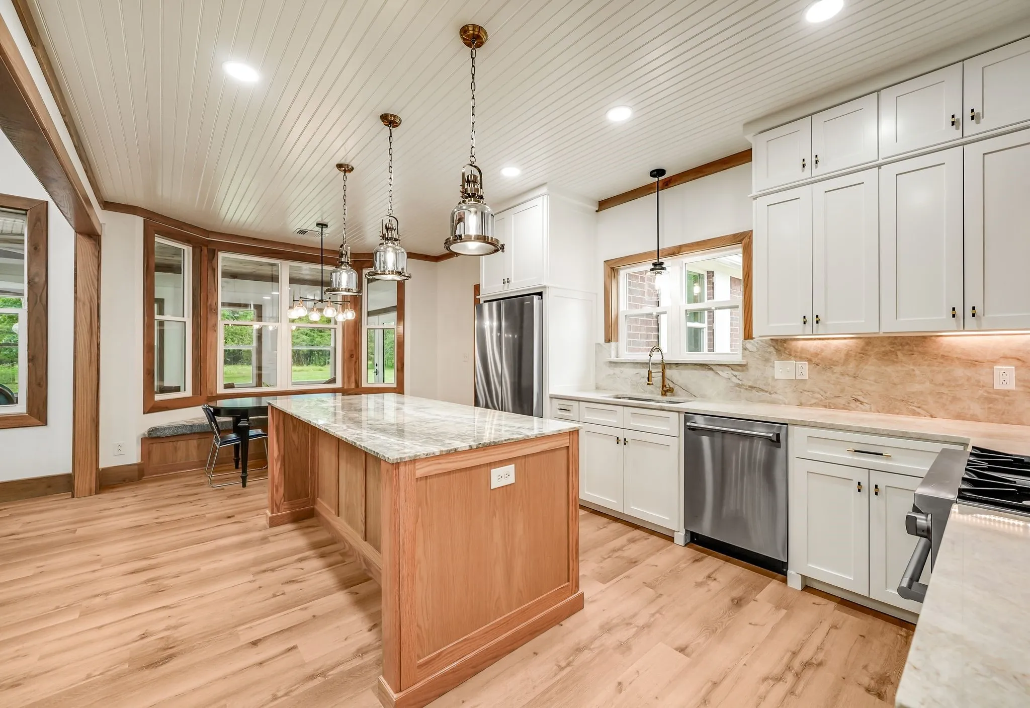 Kitchen featuring a large central island with a light-toned countertop, wood-finish flooring, white upper and lower cabinetry, stainless steel appliances, and a shiplap ceiling