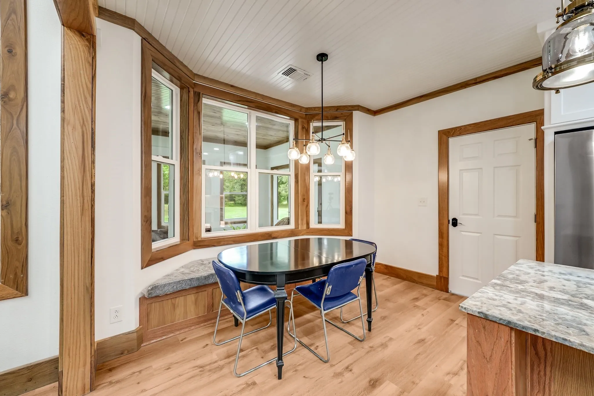 Bay window with integrated window seat, wood-finish flooring, white paneled ceilings, natural wood trim, and a contemporary chandelier