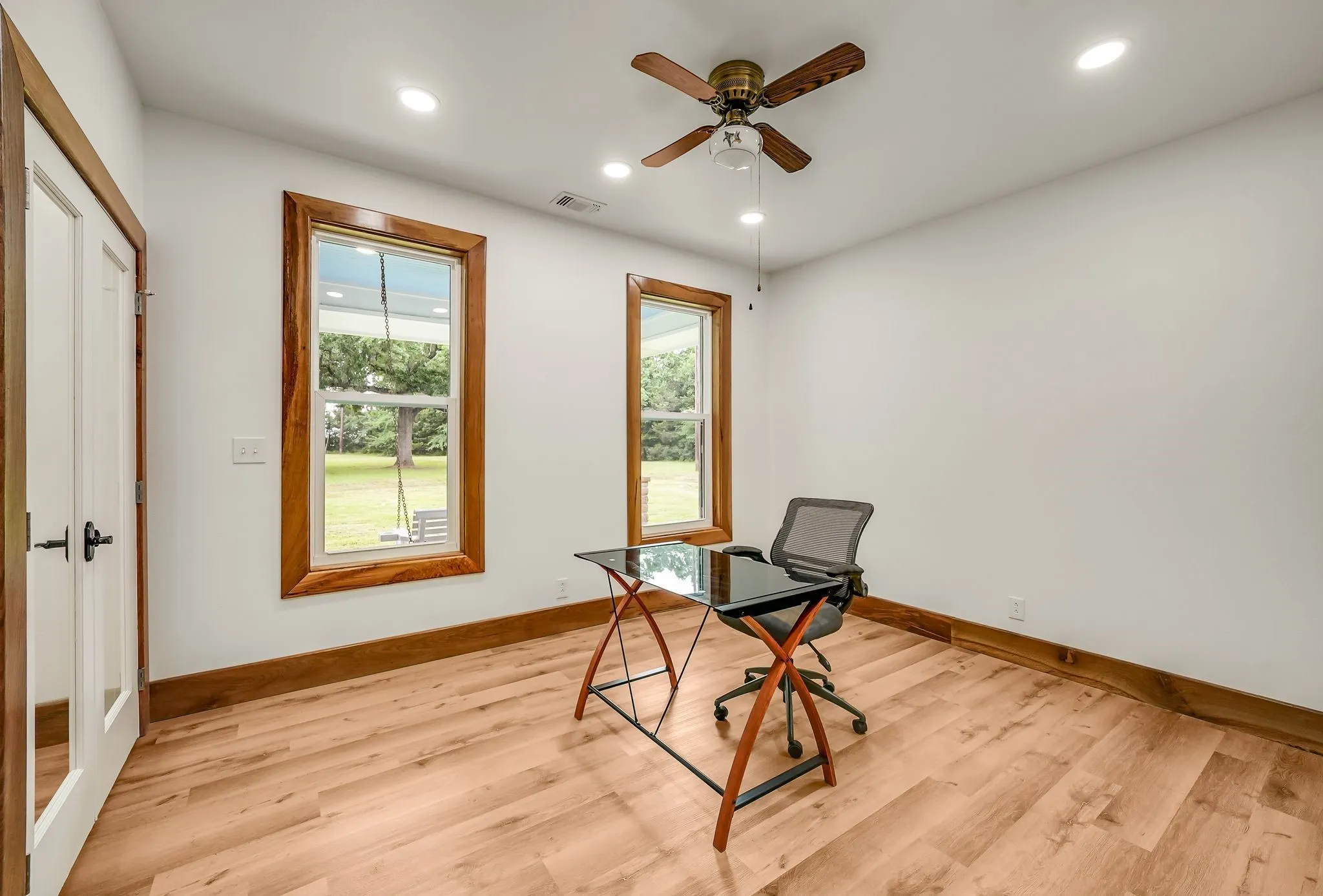Bedroom #2 on first floor featuring wood-finish flooring, two large windows with natural wood trim, white walls, and recessed lighting